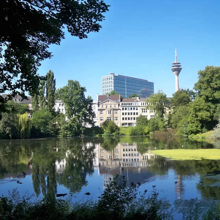Stadtsilhouette mit modernem Fernsehturm und ungewöhnlich geformten Gebäuden am Wasser.