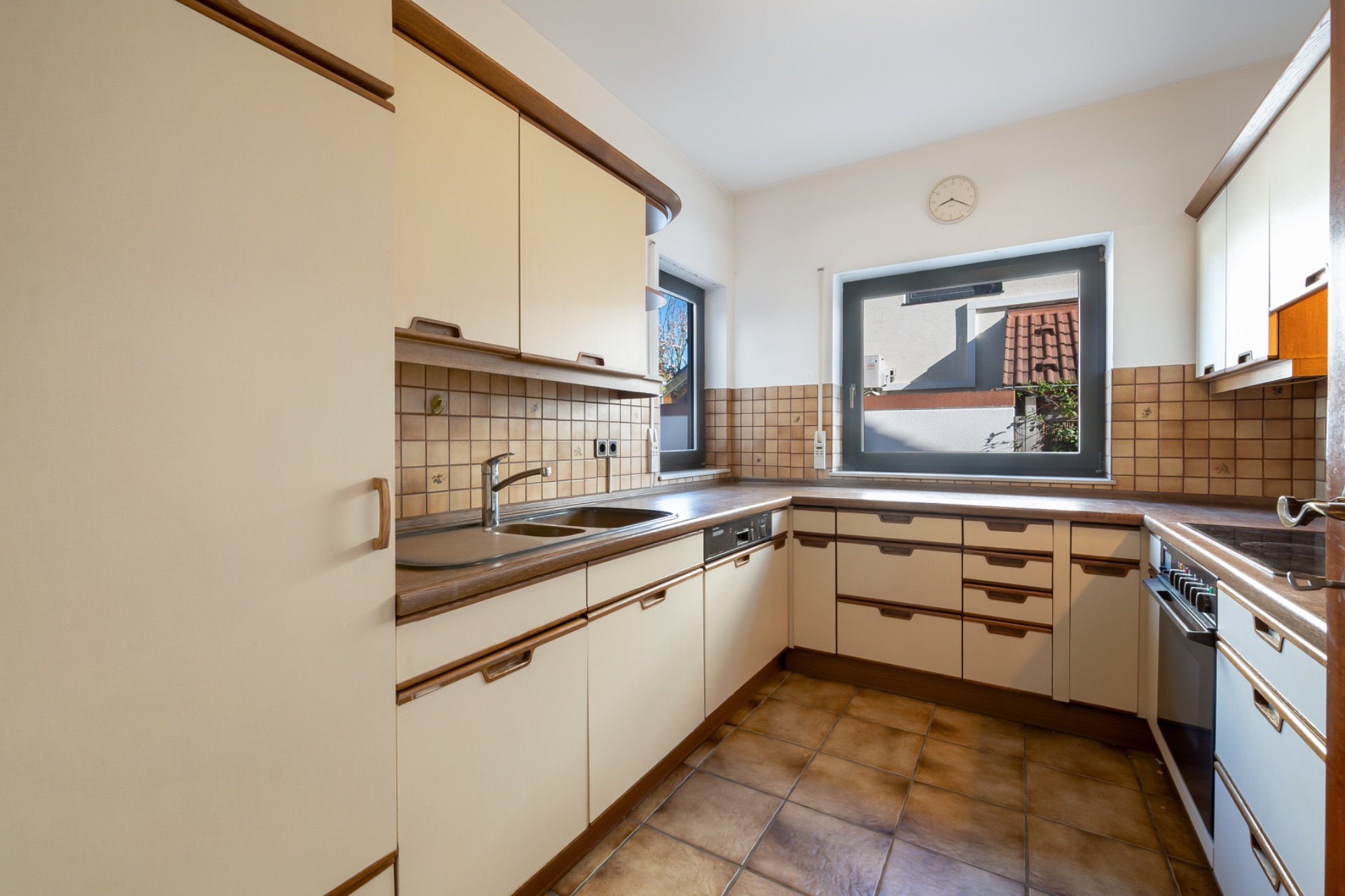Helle Einbauküche mit braunen Fliesen, großem Fenster und hellen Schränken.