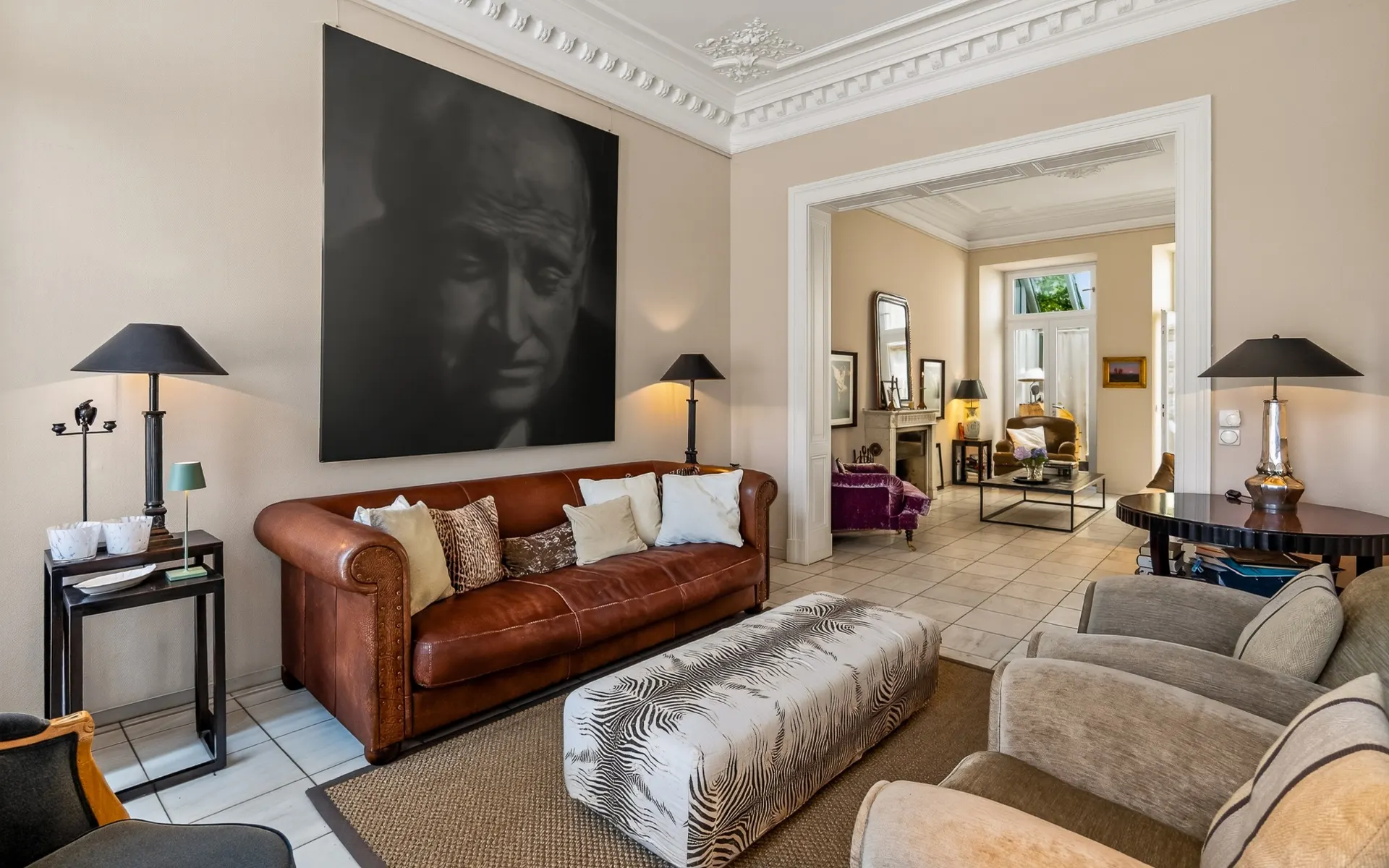 Wohnzimmer mit braunem Ledersofa, Sesseln, großem Portraitbild und dezentem Dekor.