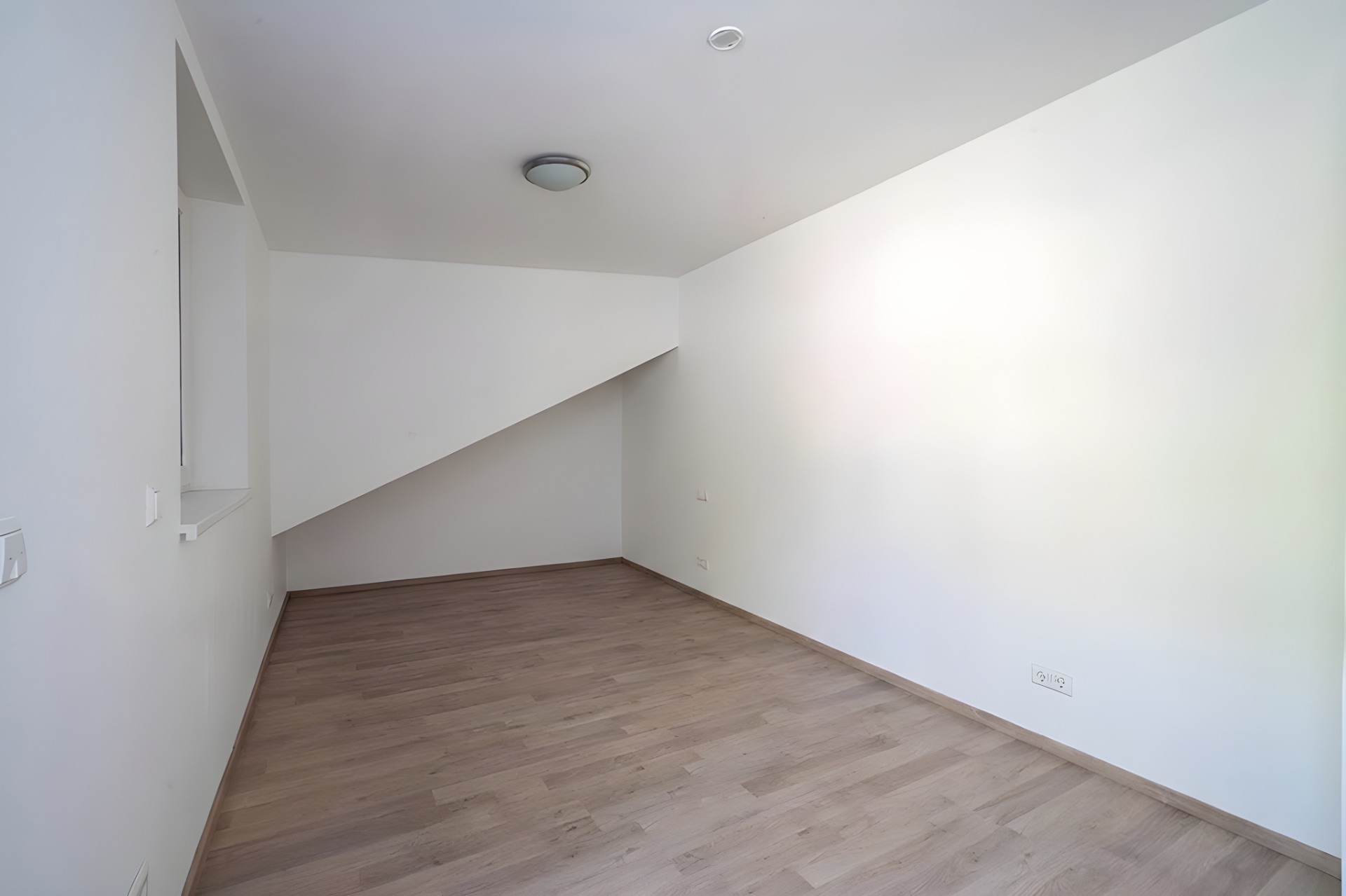 Leerer Raum mit Holzfußboden und weiß gestrichenen Wänden, Decke mit Deckenleuchte.