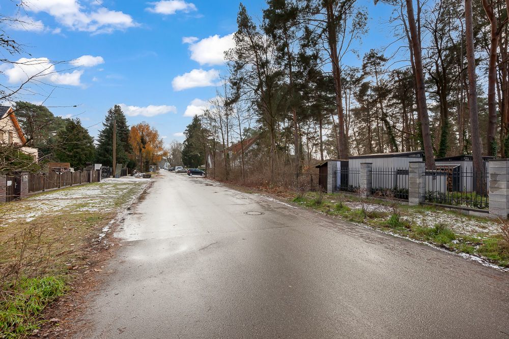 Ruhige Wohnstraße mit Bäumen, Zäunen und vereinzeltem Schnee am Straßenrand.