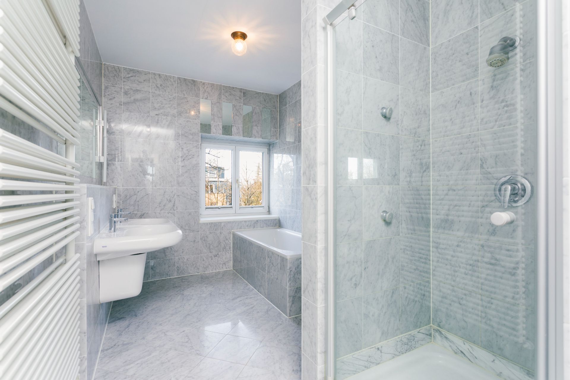 Modernes Badezimmer mit Dusche, Badewanne, Waschbecken und Fenster, alles in Marmoroptik.