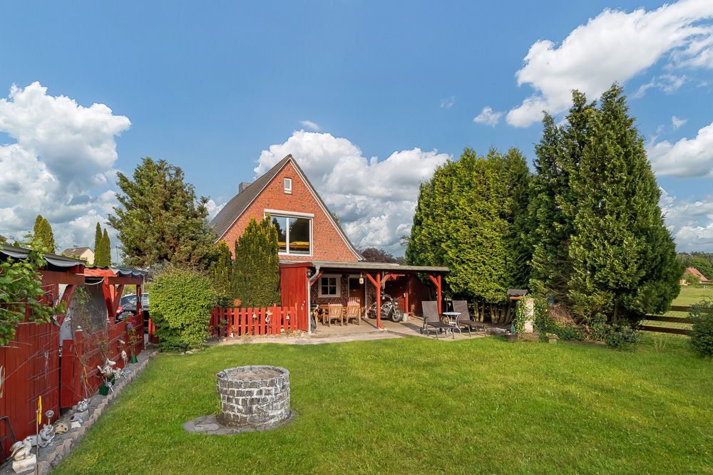 Backsteinhaus mit spitzem Dach, Terrasse und großem Garten mit Brunnen und Rasen.
