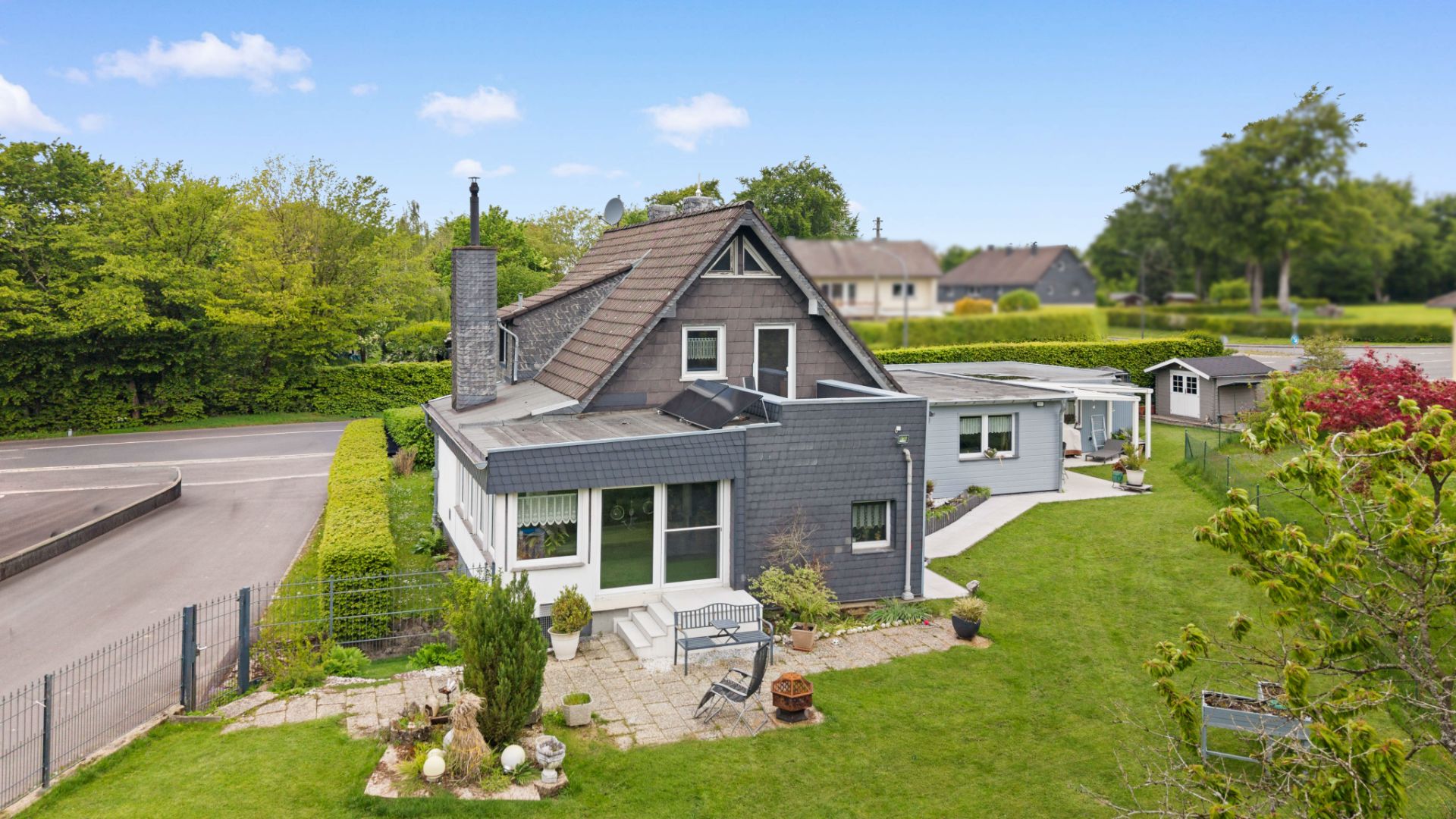Modernes Einfamilienhaus mit Garten, Terrasse und Nebengebäude auf gepflegtem Grundstück.