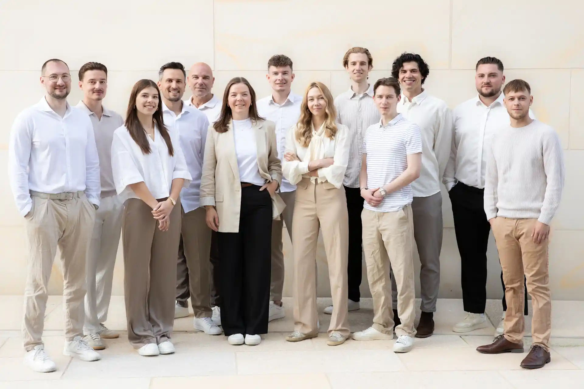 Gruppenfoto von dreizehn Menschen in heller Kleidung vor einer hellen Wand.