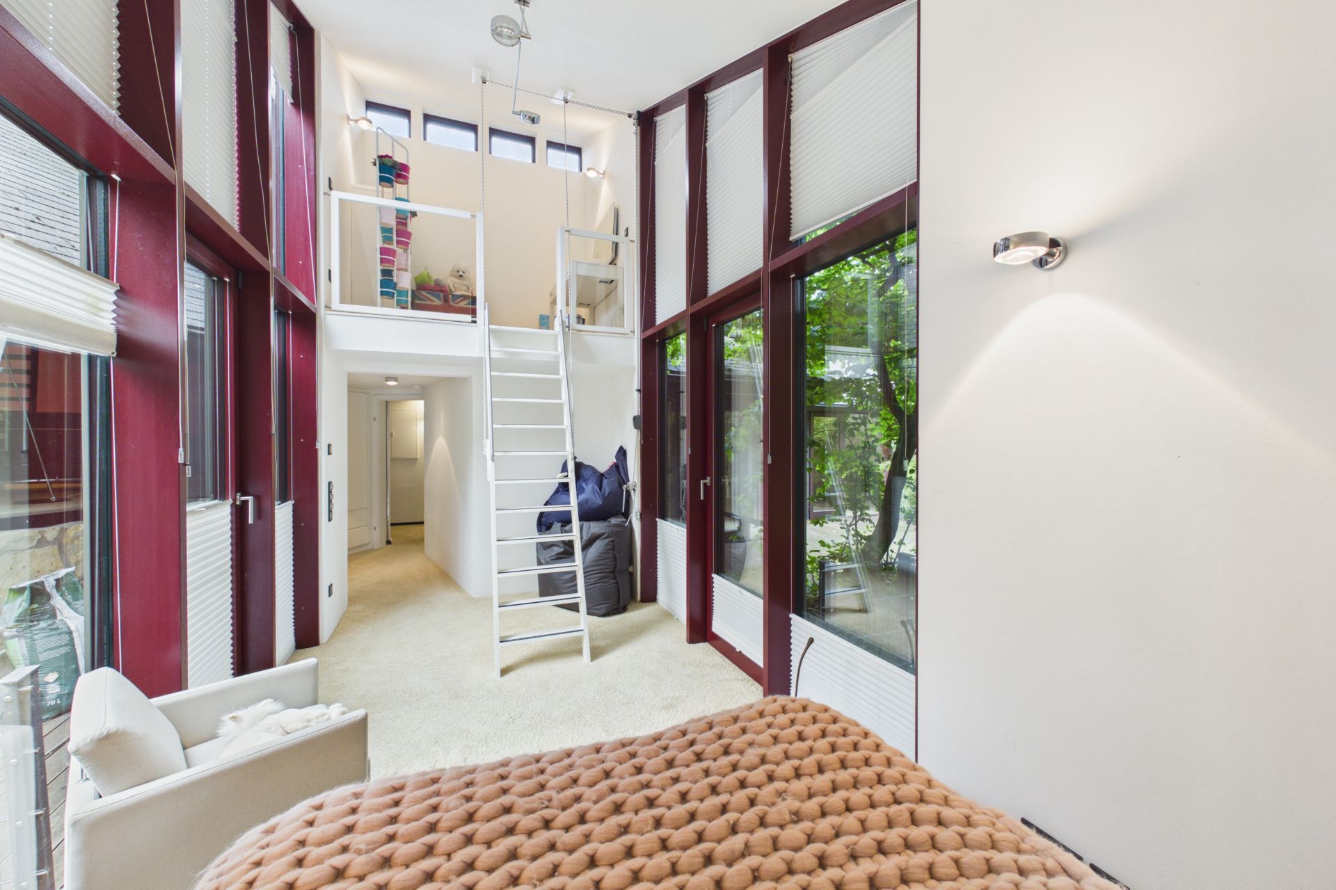 Helles Schlafzimmer mit großen Fenstern, Hochbett und Leiter, daneben Sitzbereich und Blick in den Garten.