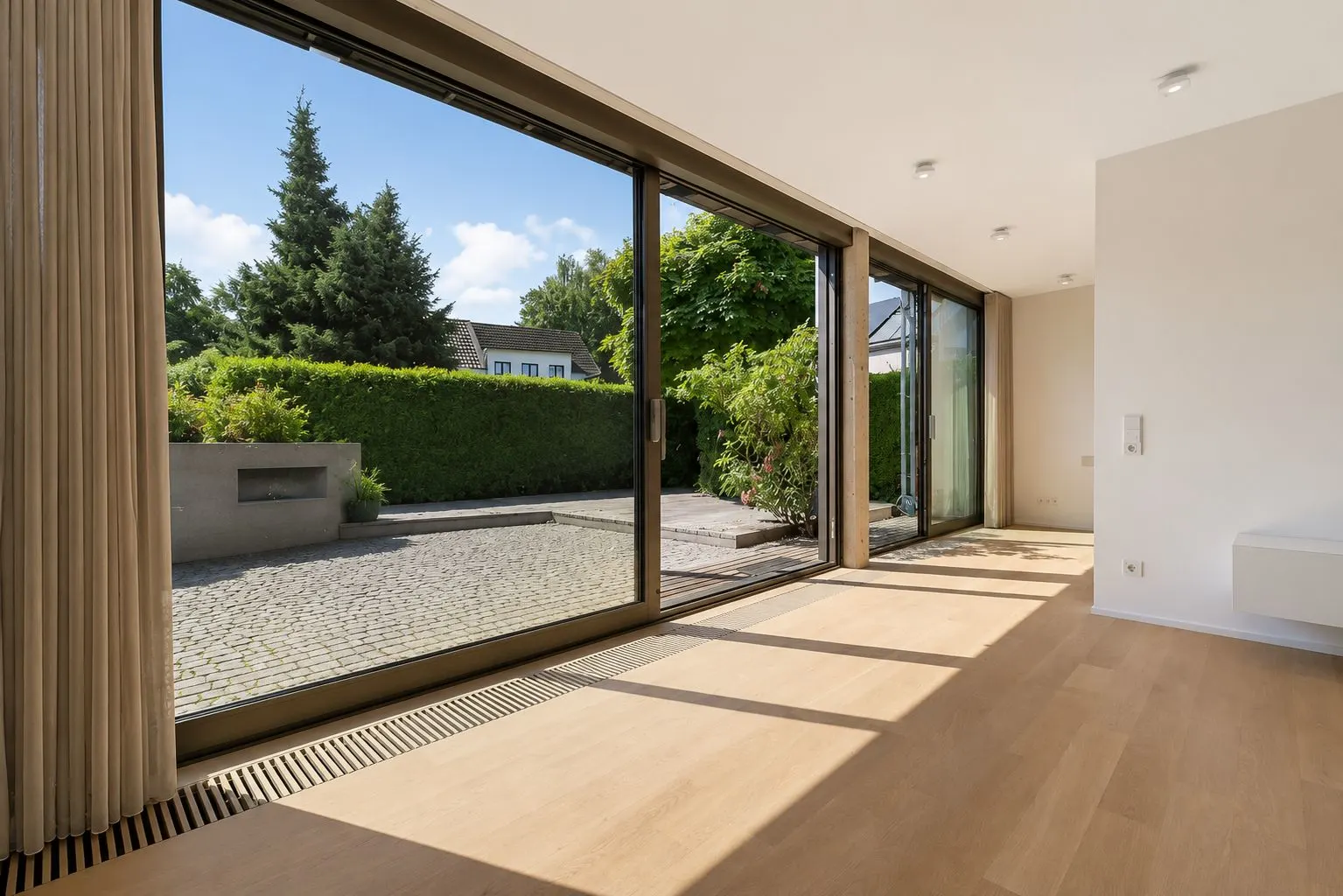 Heller Raum mit großen Glas-Schiebetüren und Blick auf einen gepflasterten Garten.