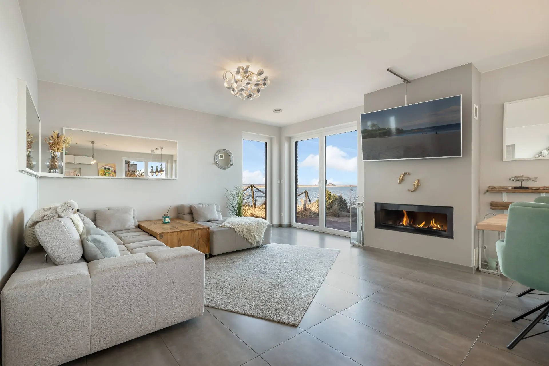 Helles Wohnzimmer mit großer Sofaecke, Kamin, Fernseher, Holztisch und Zugang zur Terrasse.