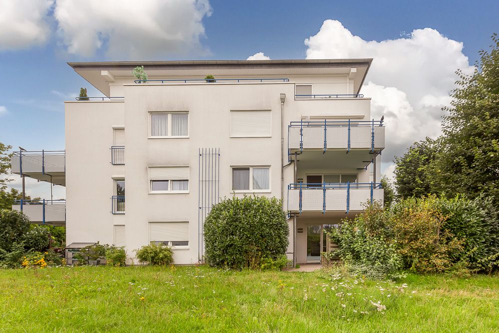 Modernes, weißes Wohngebäude mit Balkonen und großem grünen Garten im Vordergrund.
