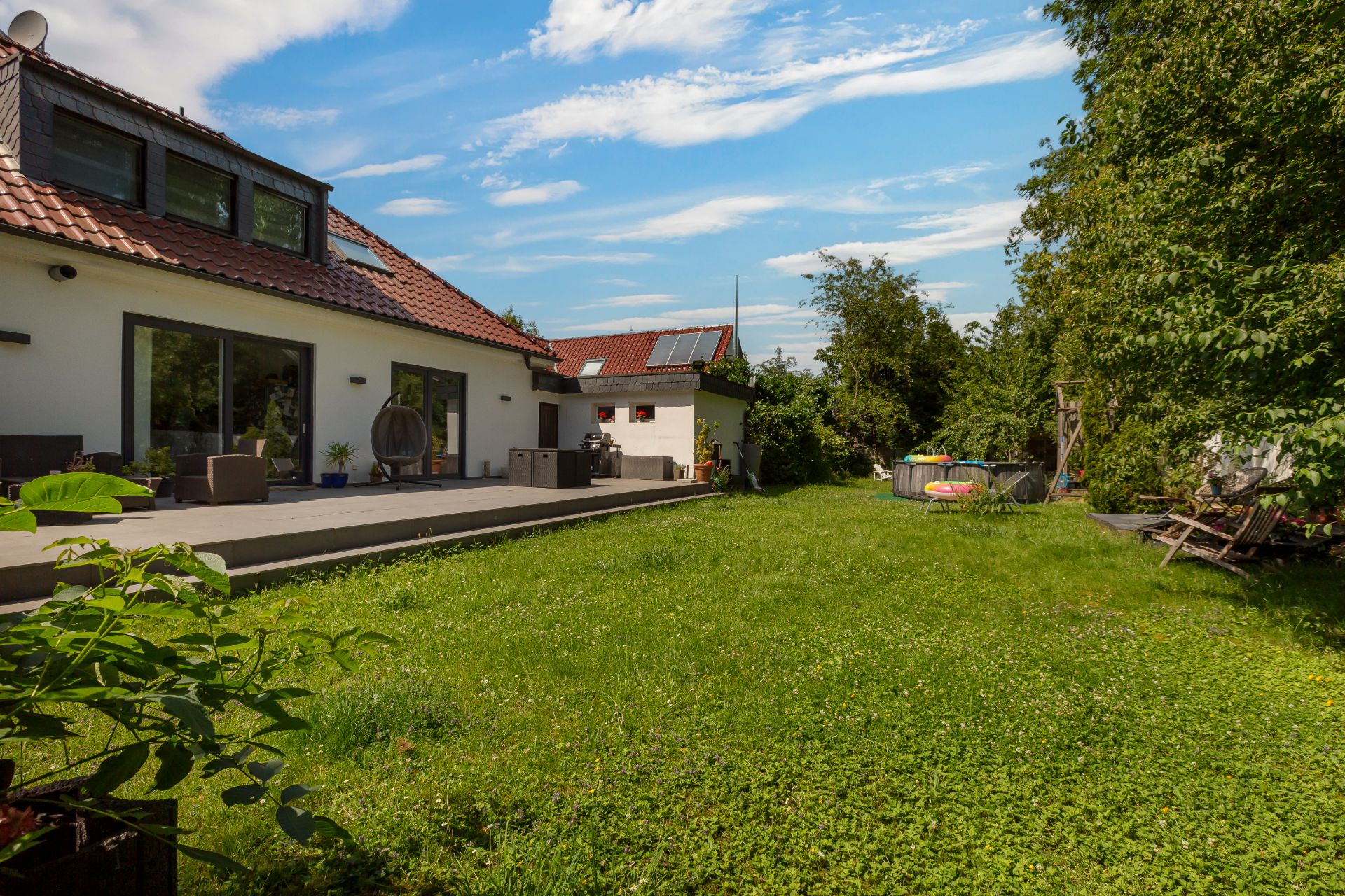 Großer grüner Garten mit Terrasse und modernem Haus im Hintergrund.