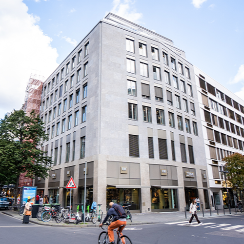 Modernes, mehrstöckiges Wohngebäude an einer Straßenecke mit großen Fenstern und Geschäften im Erdgeschoss.