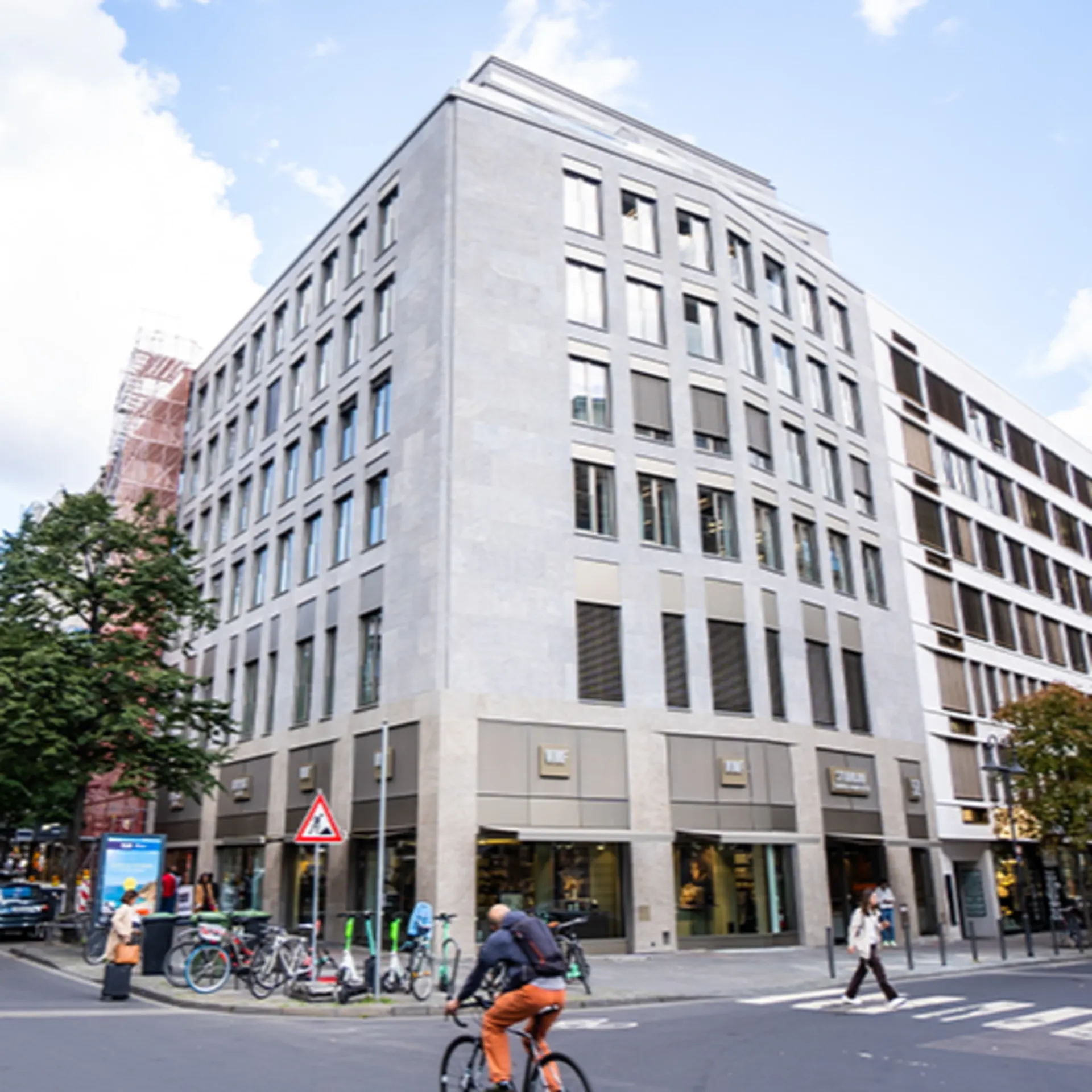 Modernes, mehrstöckiges Wohngebäude an einer Straßenecke mit großen Fenstern und Geschäften im Erdgeschoss.