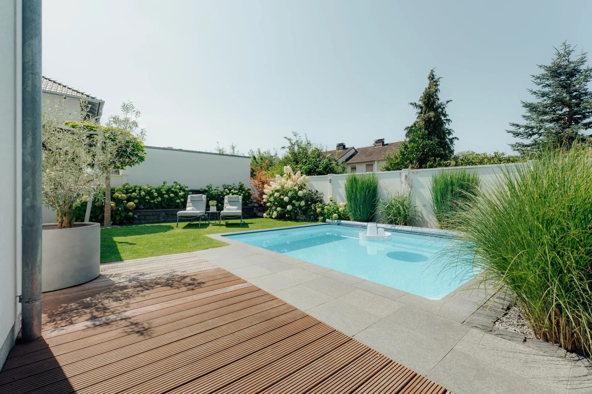Garten mit kleinem Pool, Holzterrasse, zwei Liegen und viel Grün.
