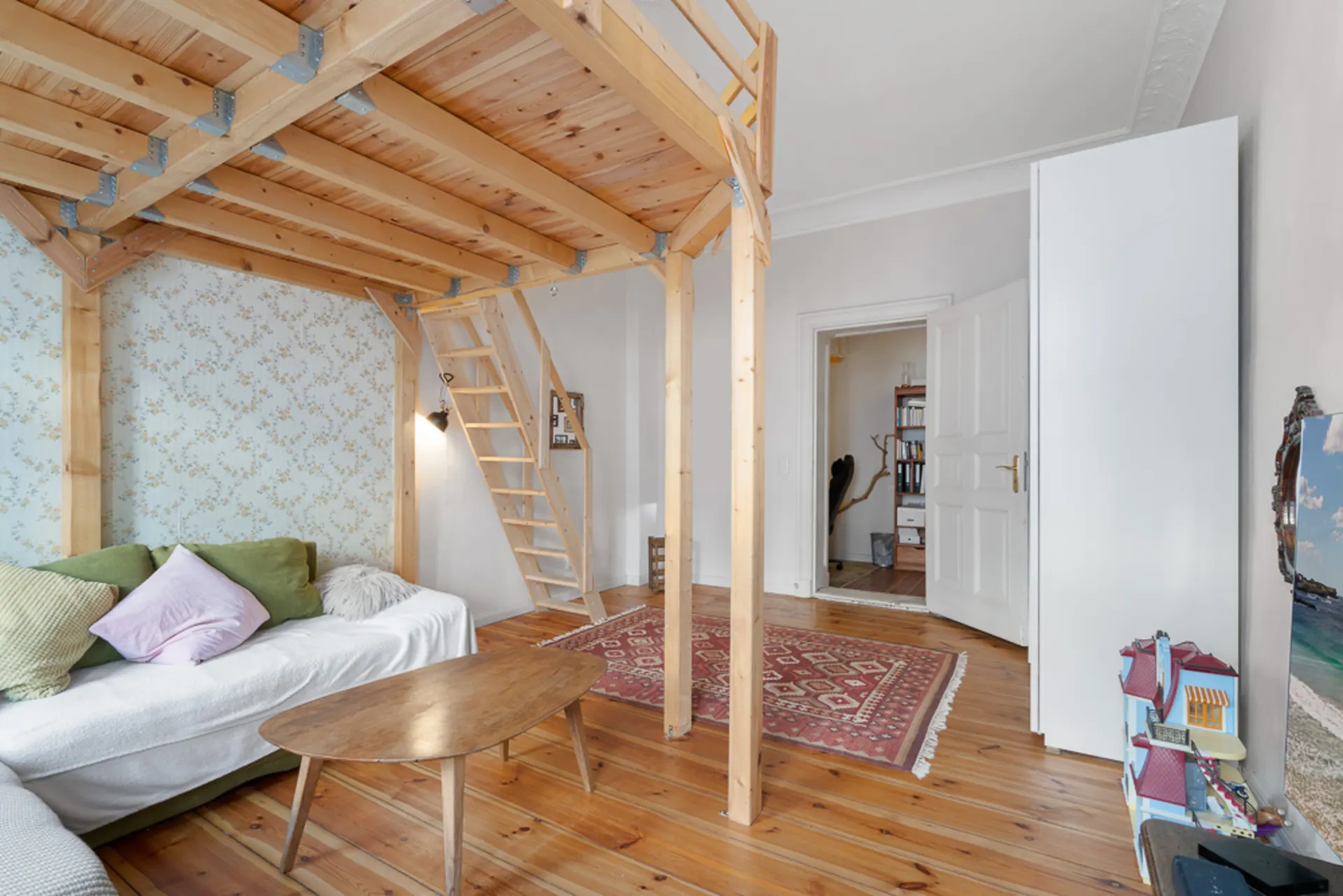 Wohnzimmer mit Hochbett aus Holz, Sofa, Couchtisch und Teppich auf Holzfußboden.
