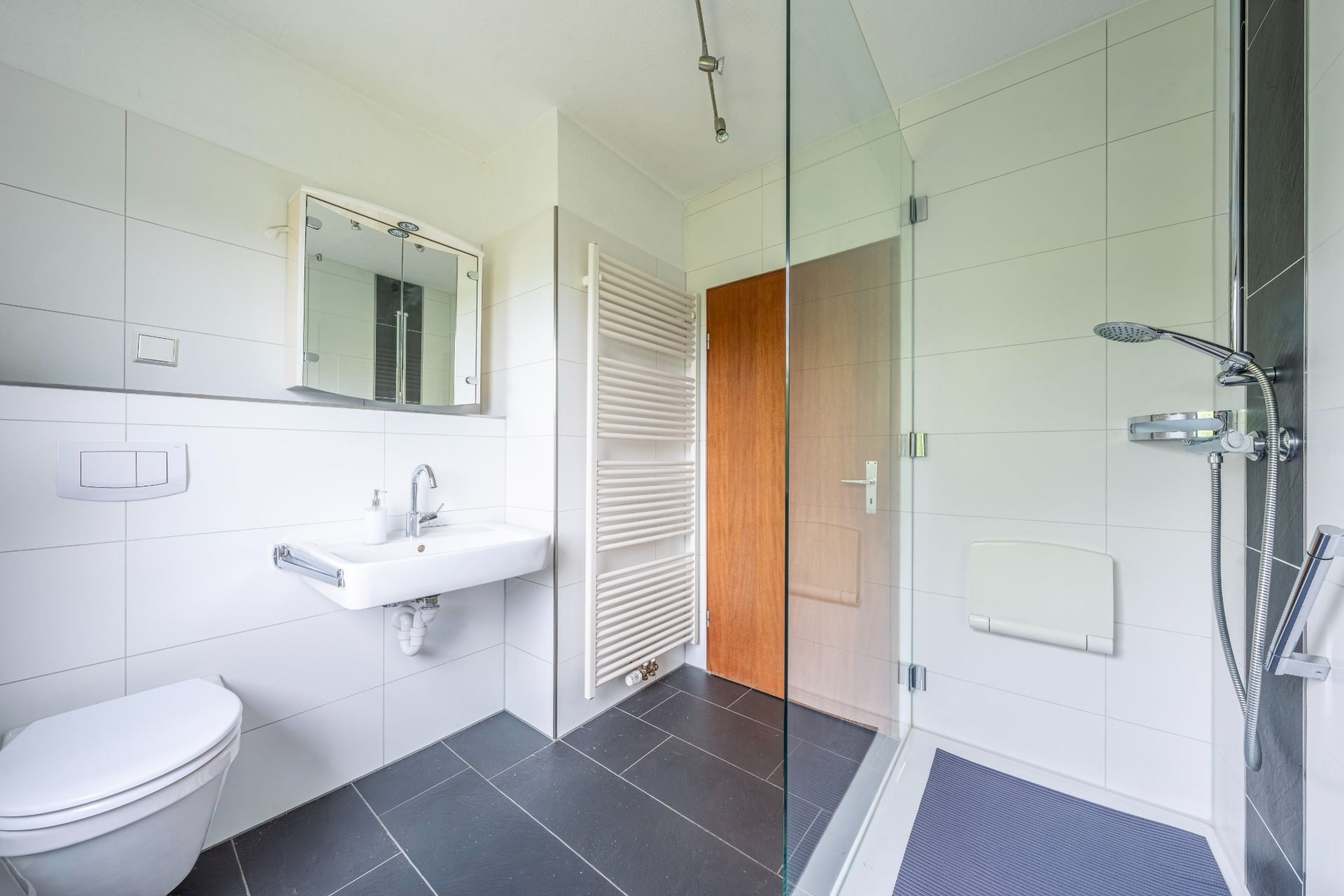 Modernes Bad mit Dusche, WC, Waschbecken, Spiegel und Handtuchheizkörper.