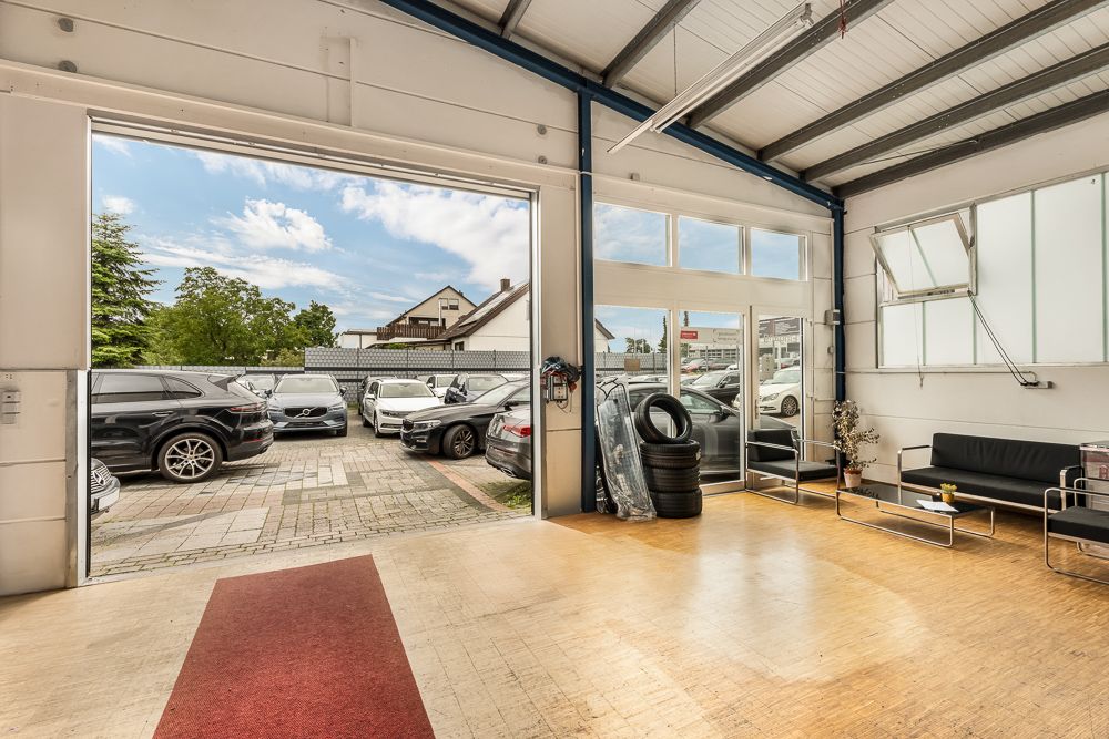 Heller Raum mit großen Fenstern, Sitzbereich, Autoreifen und Blick auf einen Parkplatz mit mehreren Autos.