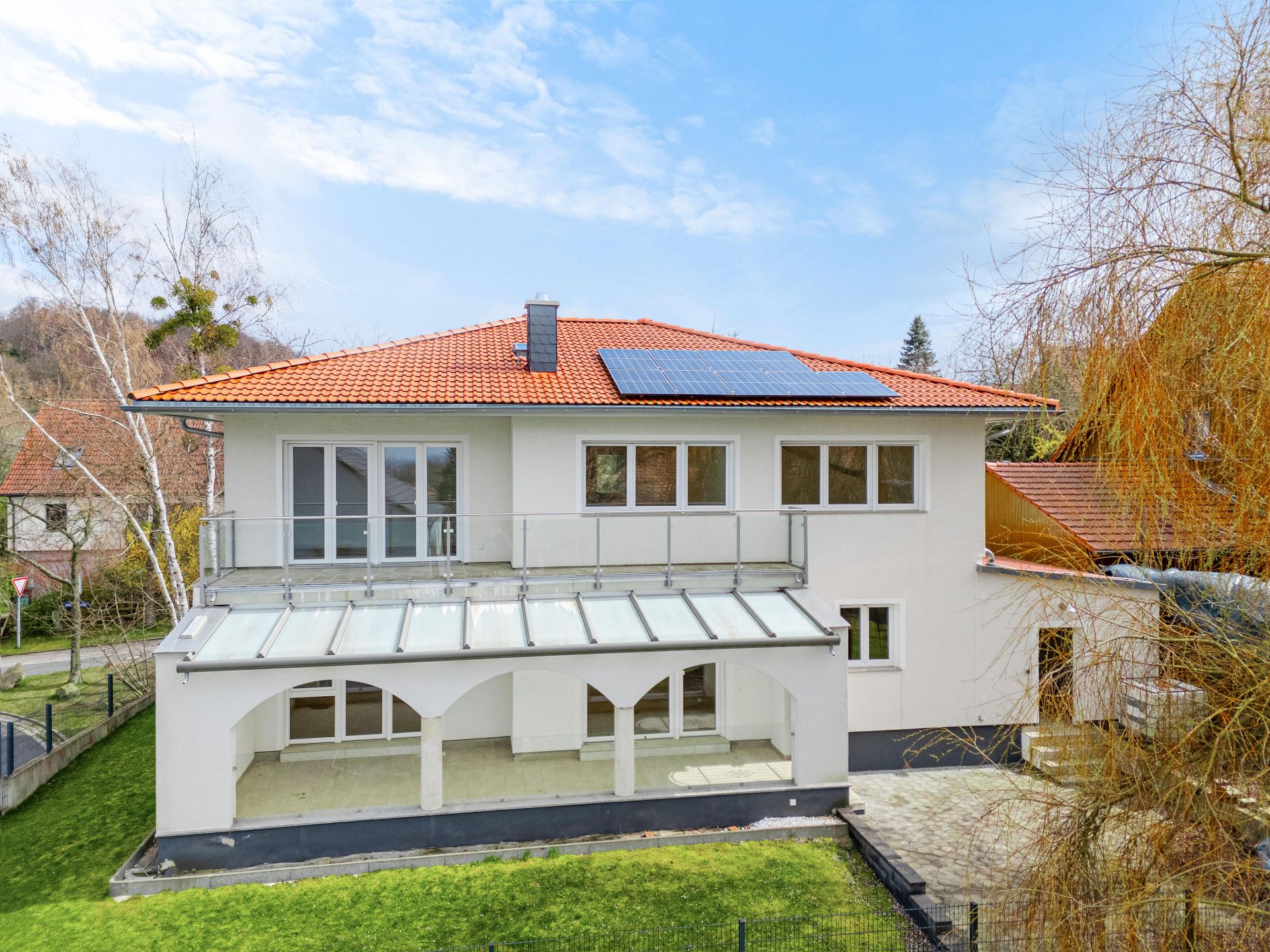 Zweistöckiges Haus mit rotem Dach, Balkon, Wintergarten und Solarpanel auf dem Dach.