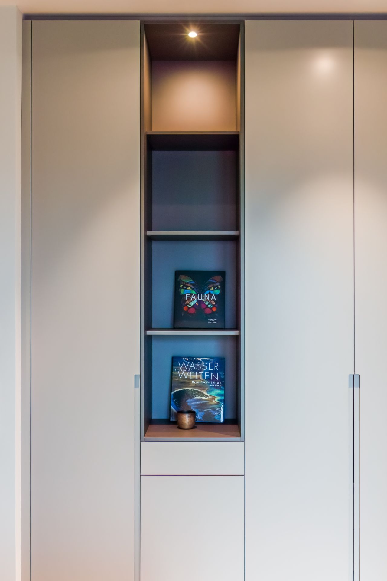 Offenes Regal in einem Schrank mit zwei Büchern und einer kleinen Kerze.