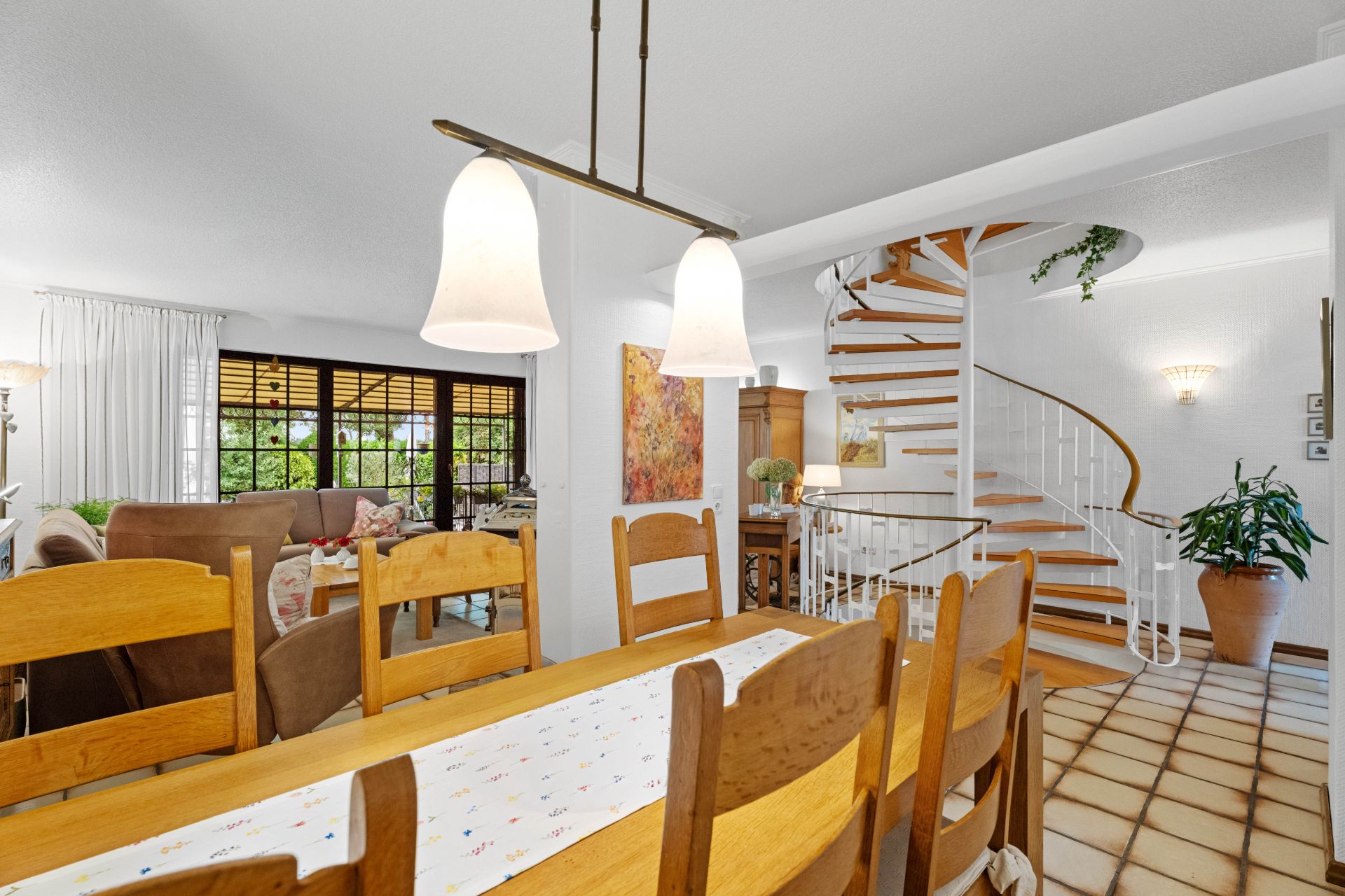 Essbereich mit Holztisch, Wohnzimmer und Wendeltreppe in einem hellen Raum.