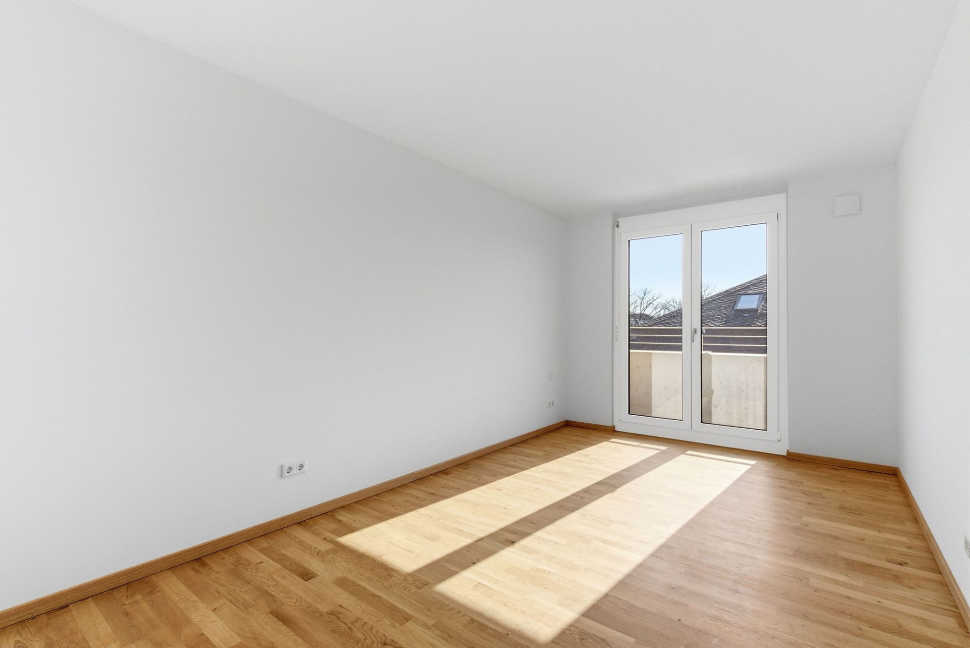 Leerer, heller Raum mit Holzfußboden und großen Fenstertüren zu einem kleinen Balkon.