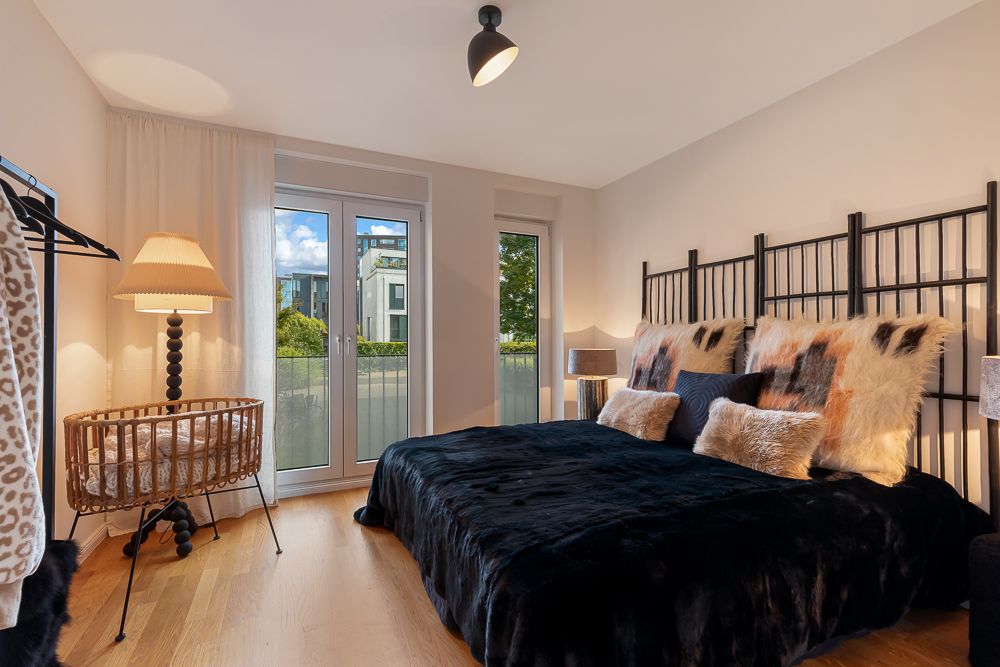 Modernes Schlafzimmer mit großem Bett, Pelzkissen, Schreibtisch, Lampe und Zugang zum Balkon.