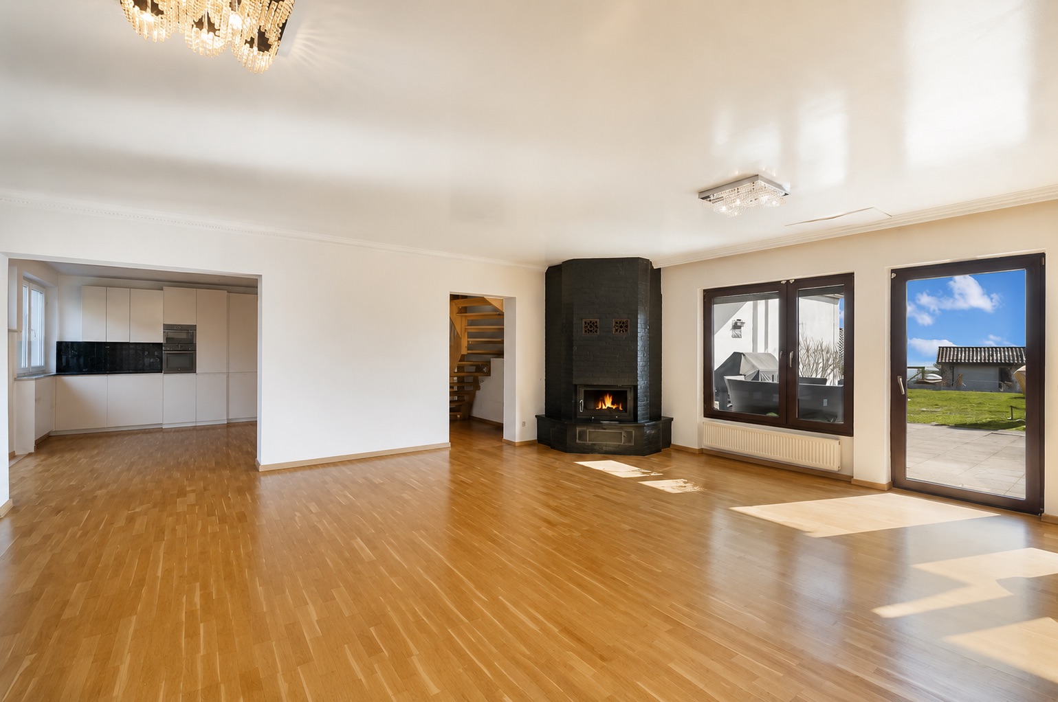 Helles Wohnzimmer mit Parkettboden, Kamin, großen Fenstern und Zugang zur Terrasse.