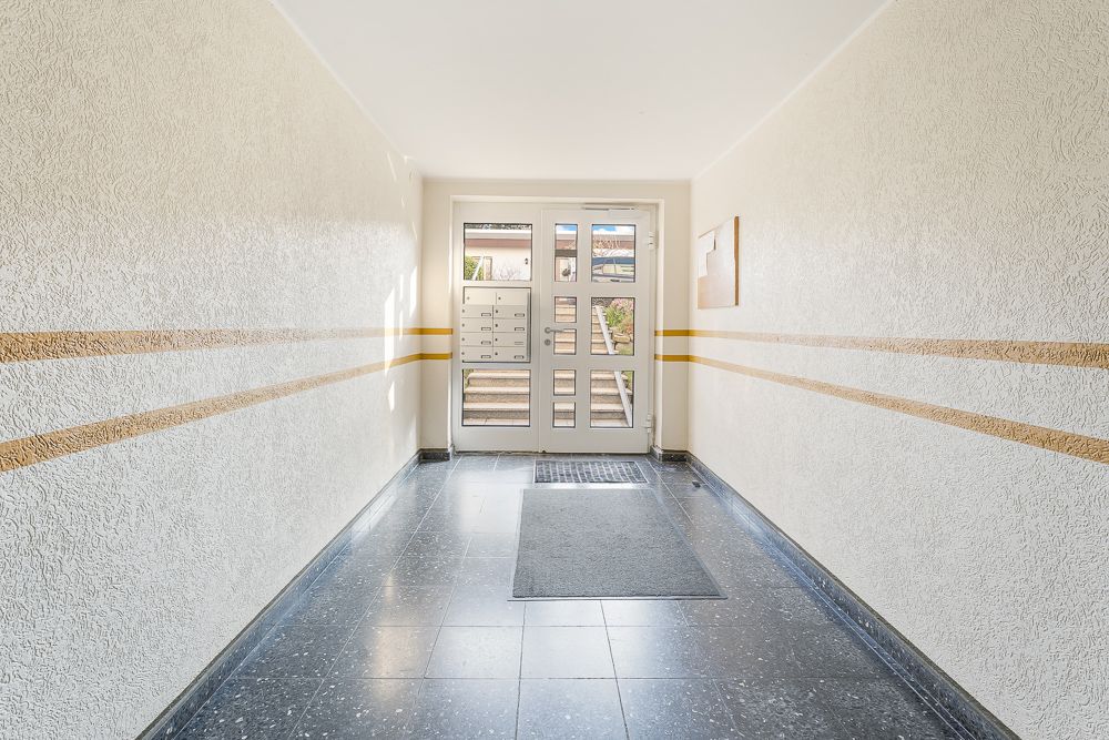 Heller Hausflur mit gelben Streifen an den Wänden und Briefkästen neben der Eingangstür.