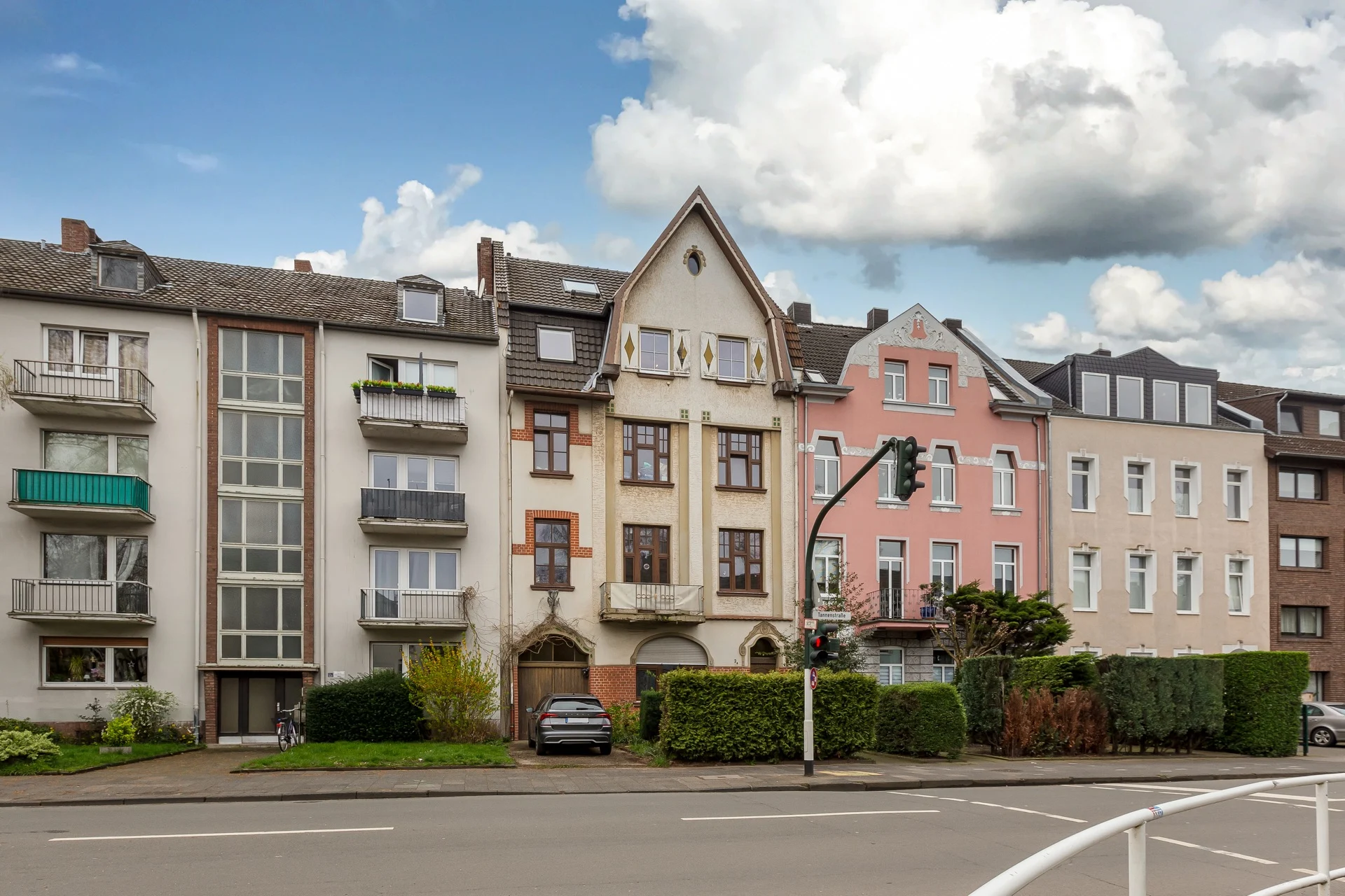 Mehrere Wohngebäude mit Balkonen und Vorgärten an einer Straße bei Tageslicht.