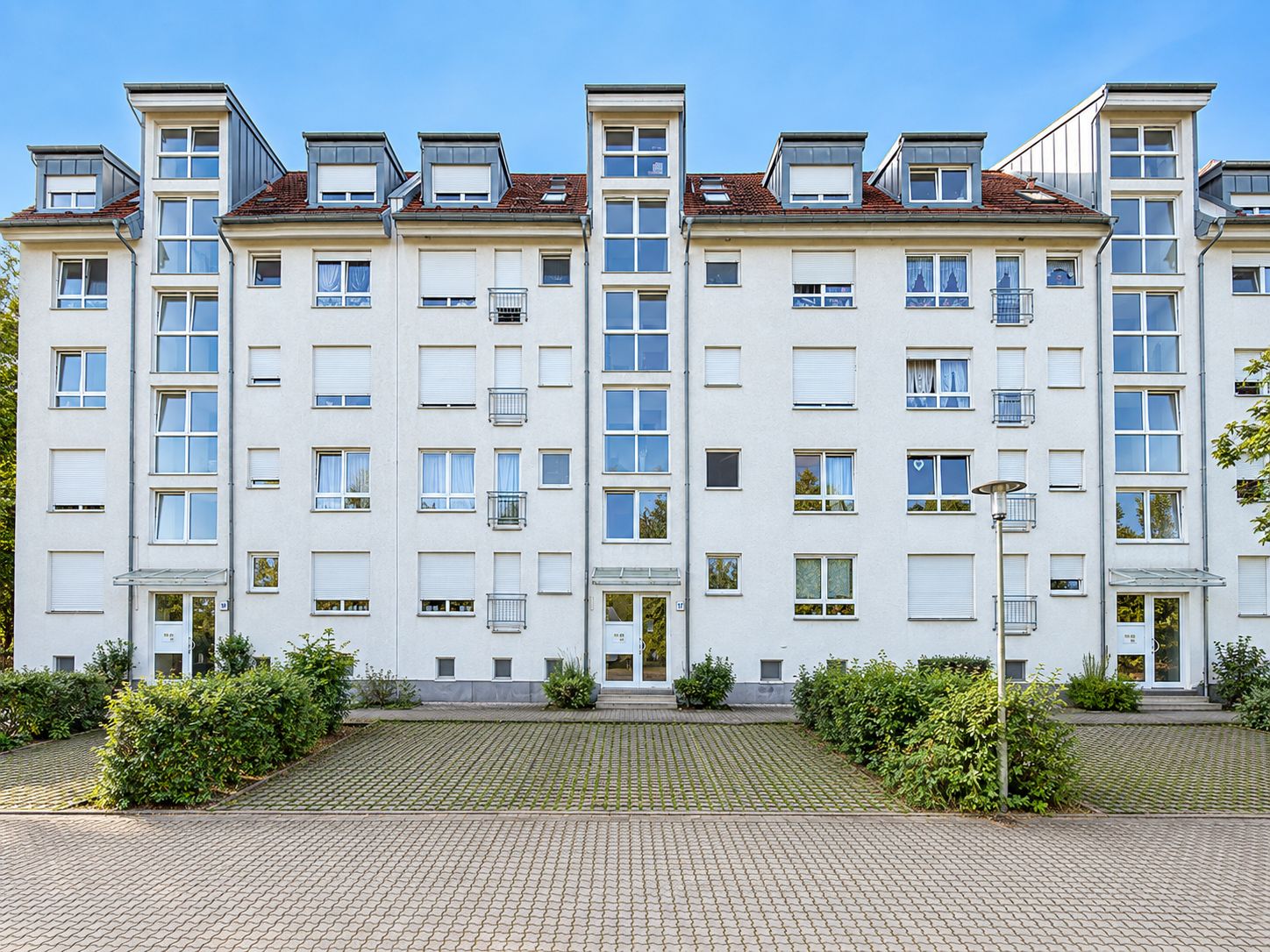 Mehrstöckiges Wohnhaus mit weißen Fassaden, vielen Fenstern und begrüntem Vorplatz.