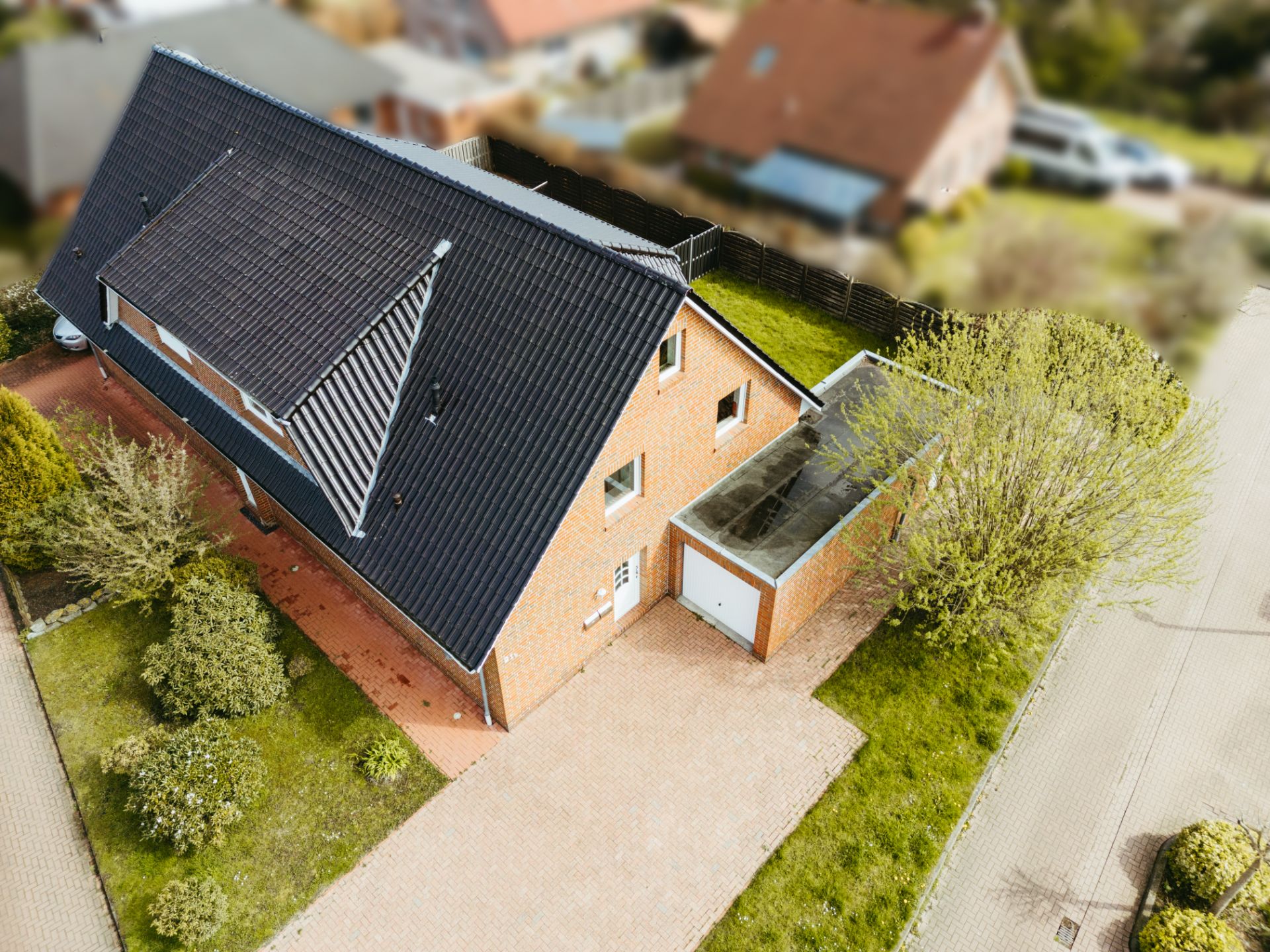 Luftaufnahme eines Einfamilienhauses mit schwarzem Dach, Garage und Garten, an einer Straße gelegen.