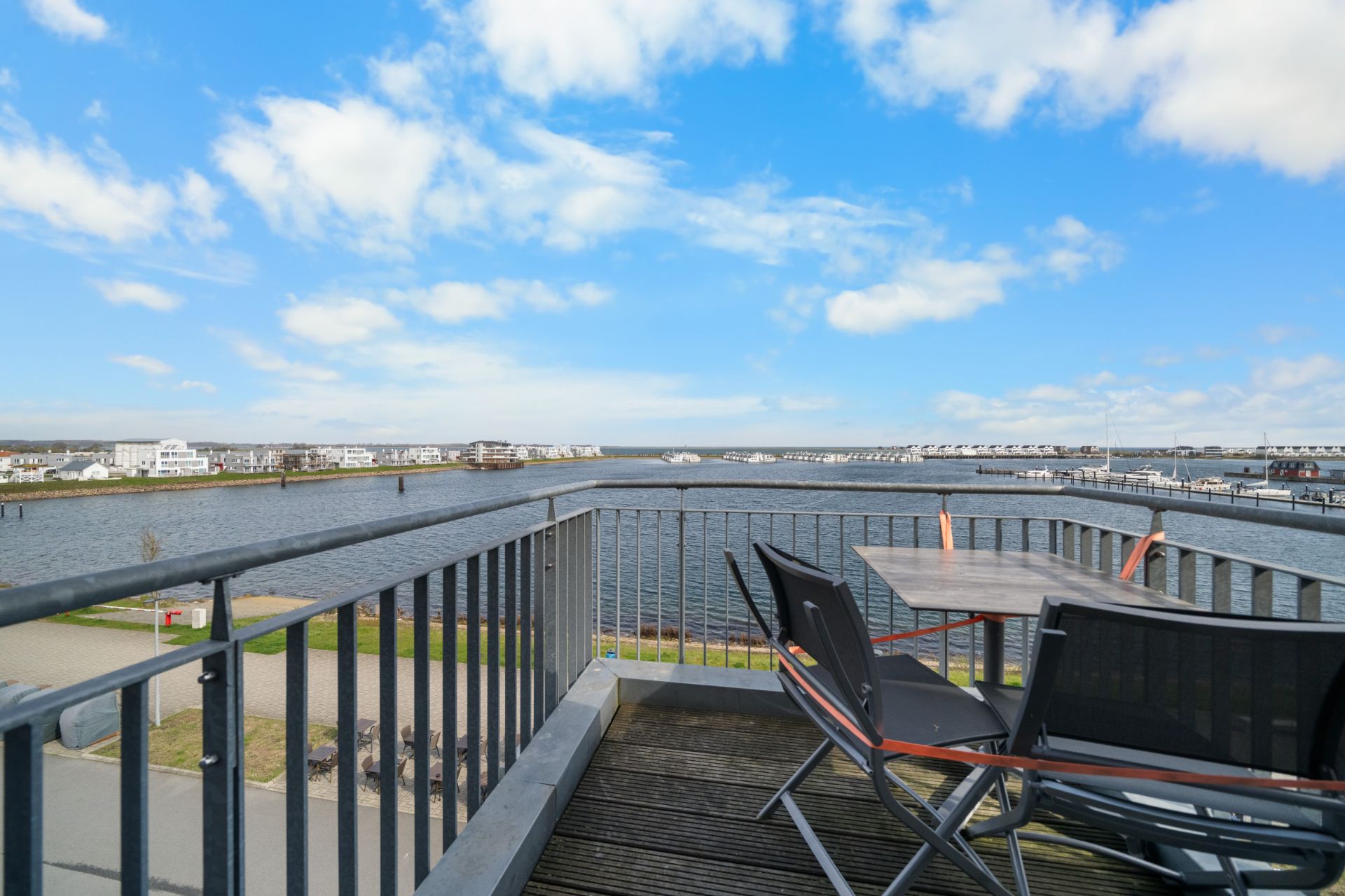 Balkon mit Tisch und Stühlen, Blick auf Wasser, Ufer und blauem Himmel.