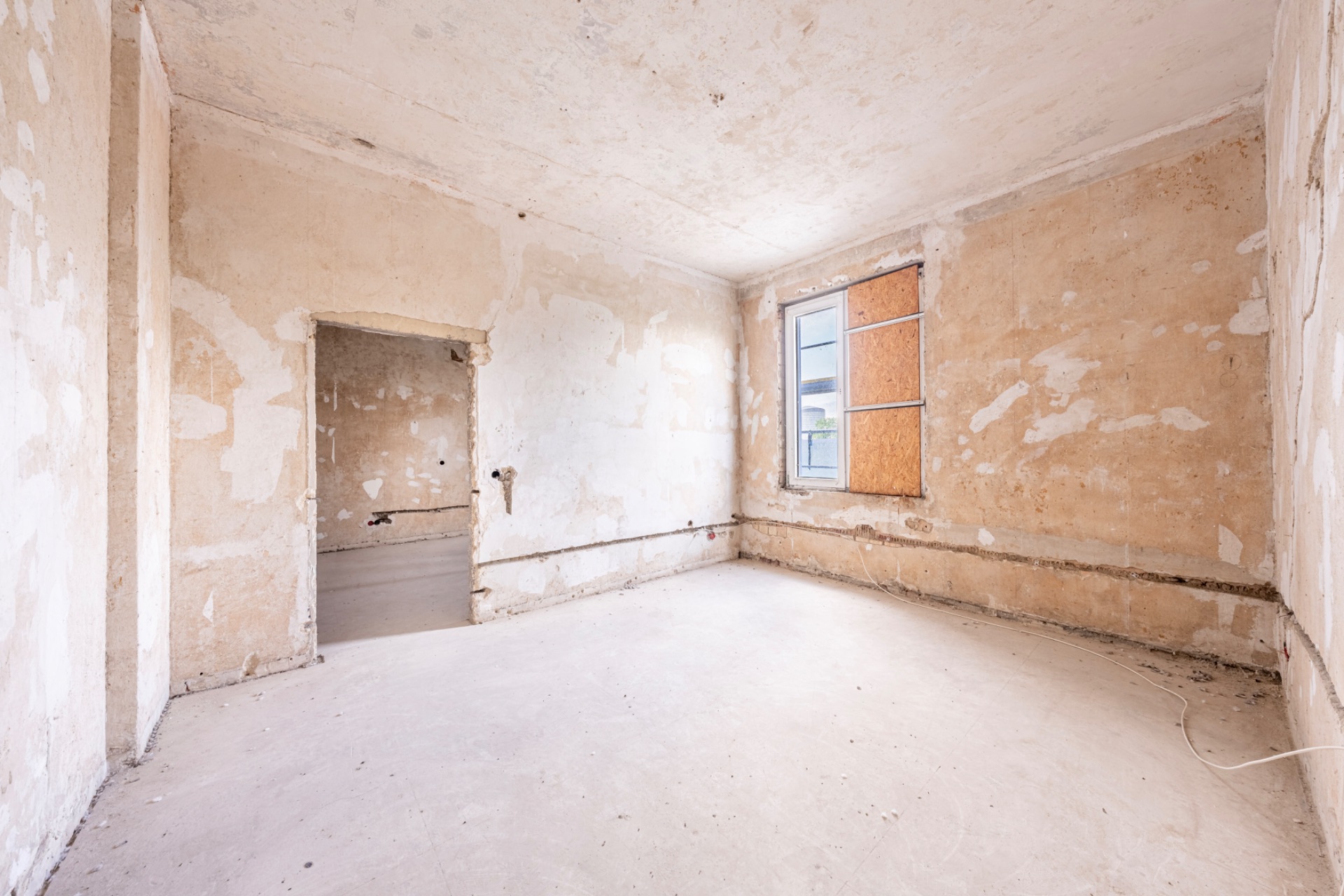 Leerer Raum mit abgenutzten Wänden, offenem Fenster und sichtbaren Rohren an der Wand.