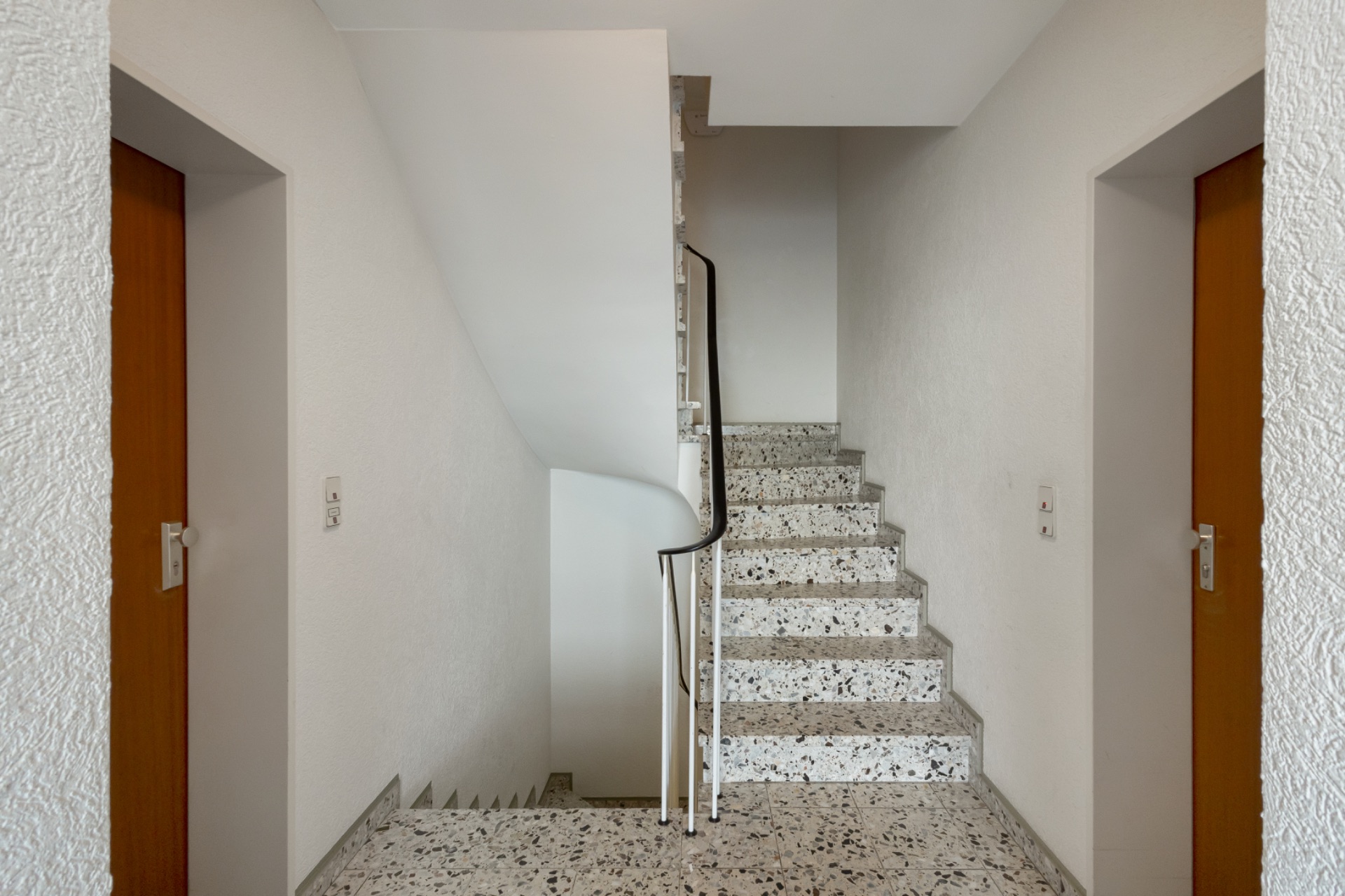 Treppenhaus mit Terrazzo-Treppe und zwei Holztüren auf jeder Seite.