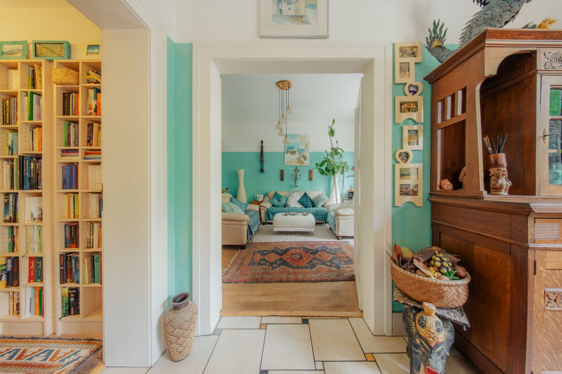 Blick durch Flur auf Wohnzimmer mit Sofas, Teppichen, Bücherregal und Holzschrank.