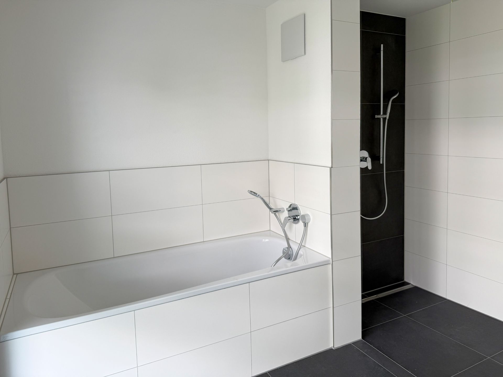 Modernes Badezimmer mit Badewanne und begehbarer Dusche, weiße Wandfliesen.