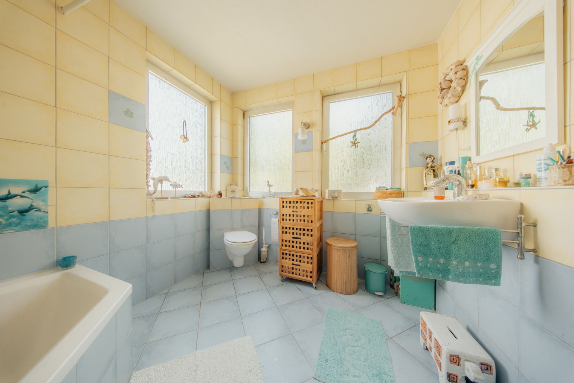 Helles Badezimmer mit Badewanne, WC, Waschbecken und drei großen Fenstern.
