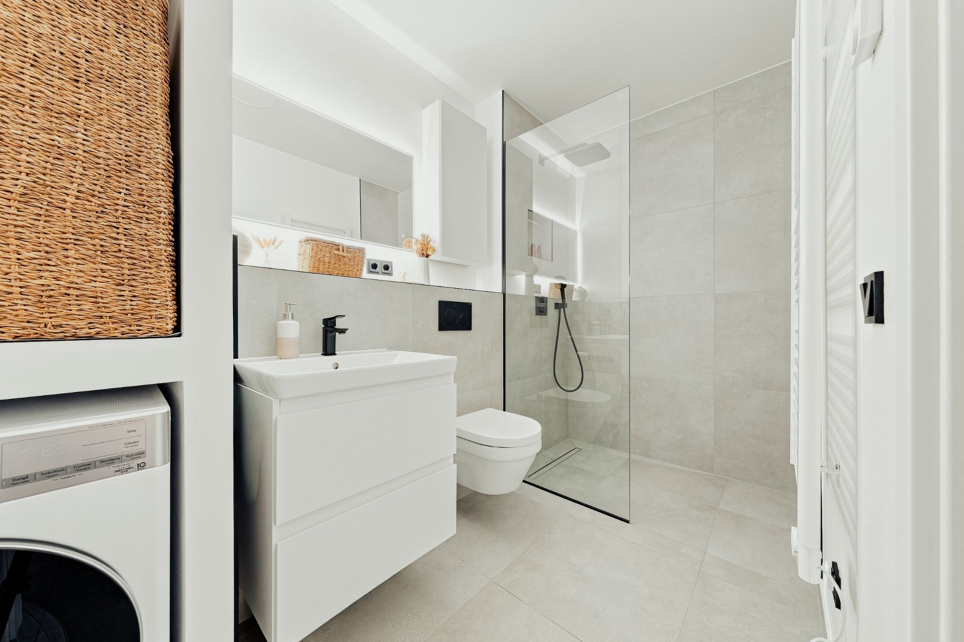Modernes Badezimmer mit Waschbecken, WC, offener Dusche und Waschmaschine.