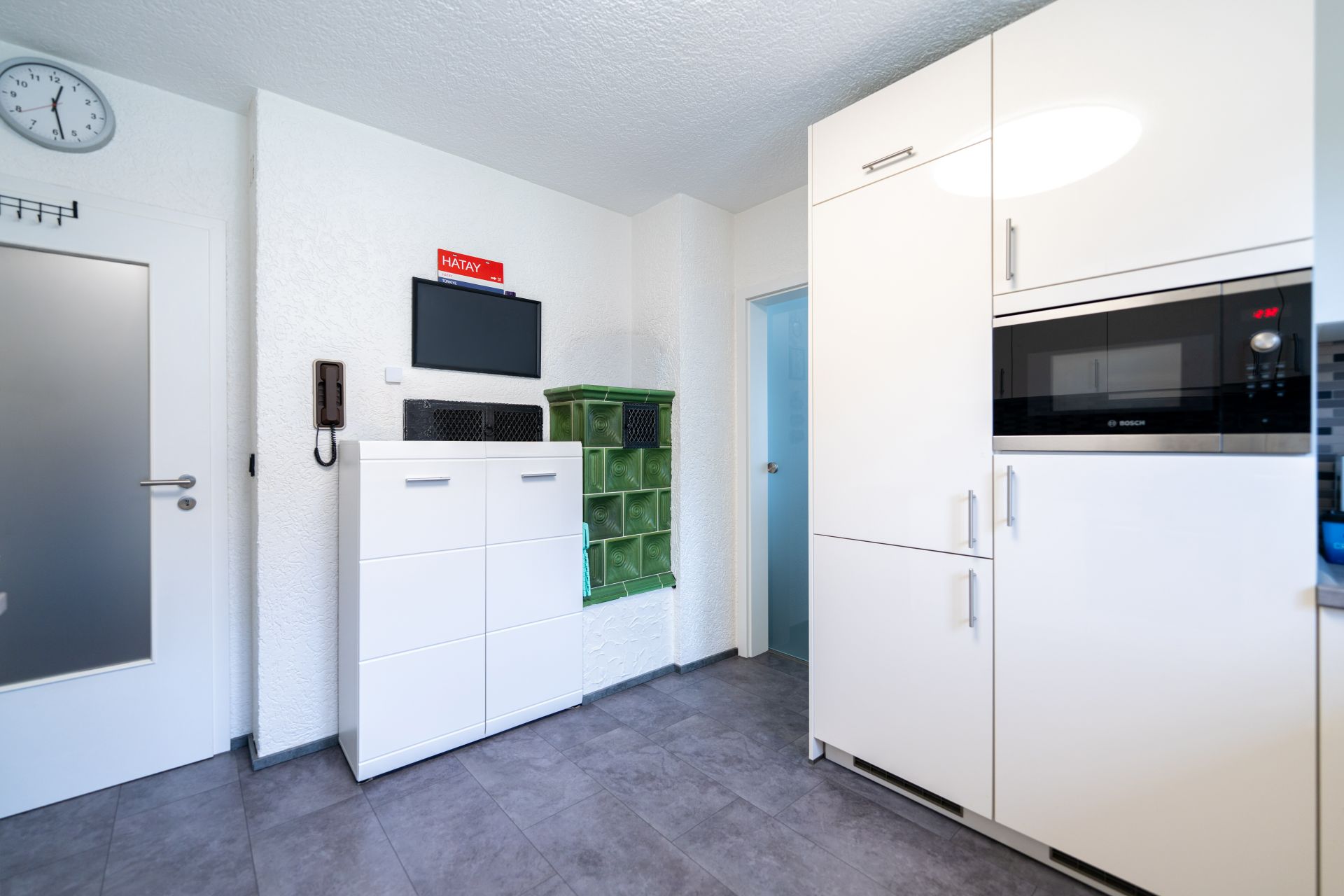 Moderne Küche mit weißen Schränken, Mikrowelle und grünem Kachelherd an der Wand.