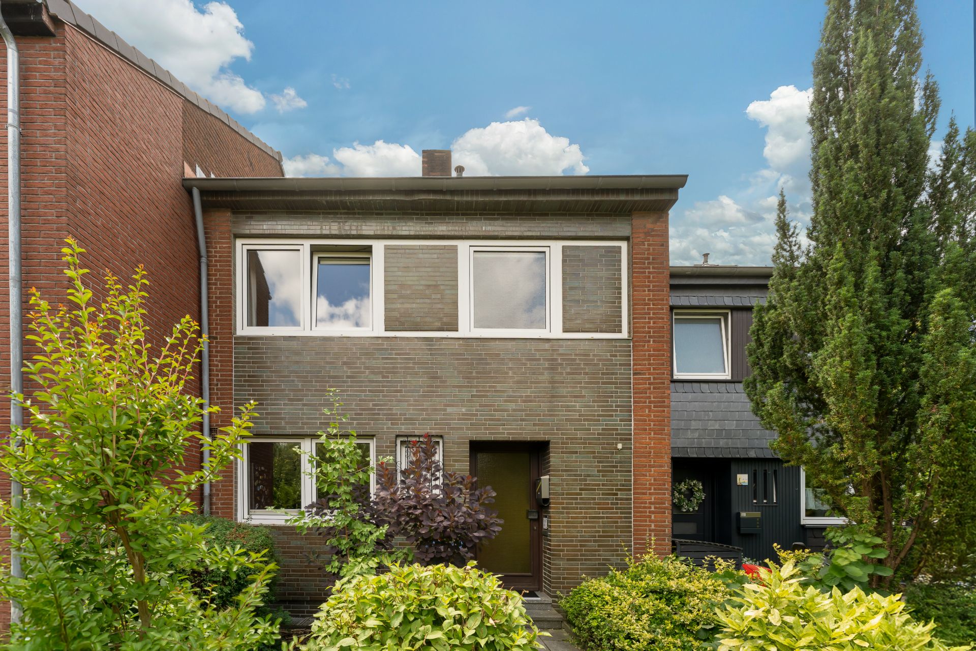 Vorderansicht eines zweistöckigen Hauses mit Ziegelmauerwerk und Vorgarten.