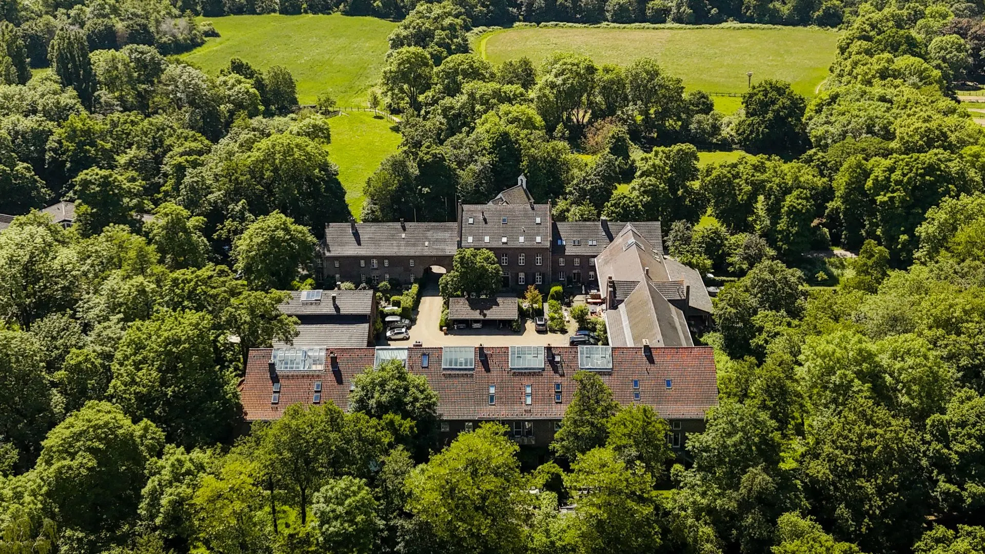 Luftaufnahme eines großen Wohngebäudekomplexes mit Innenhof, umgeben von vielen Bäumen und Grünflächen.