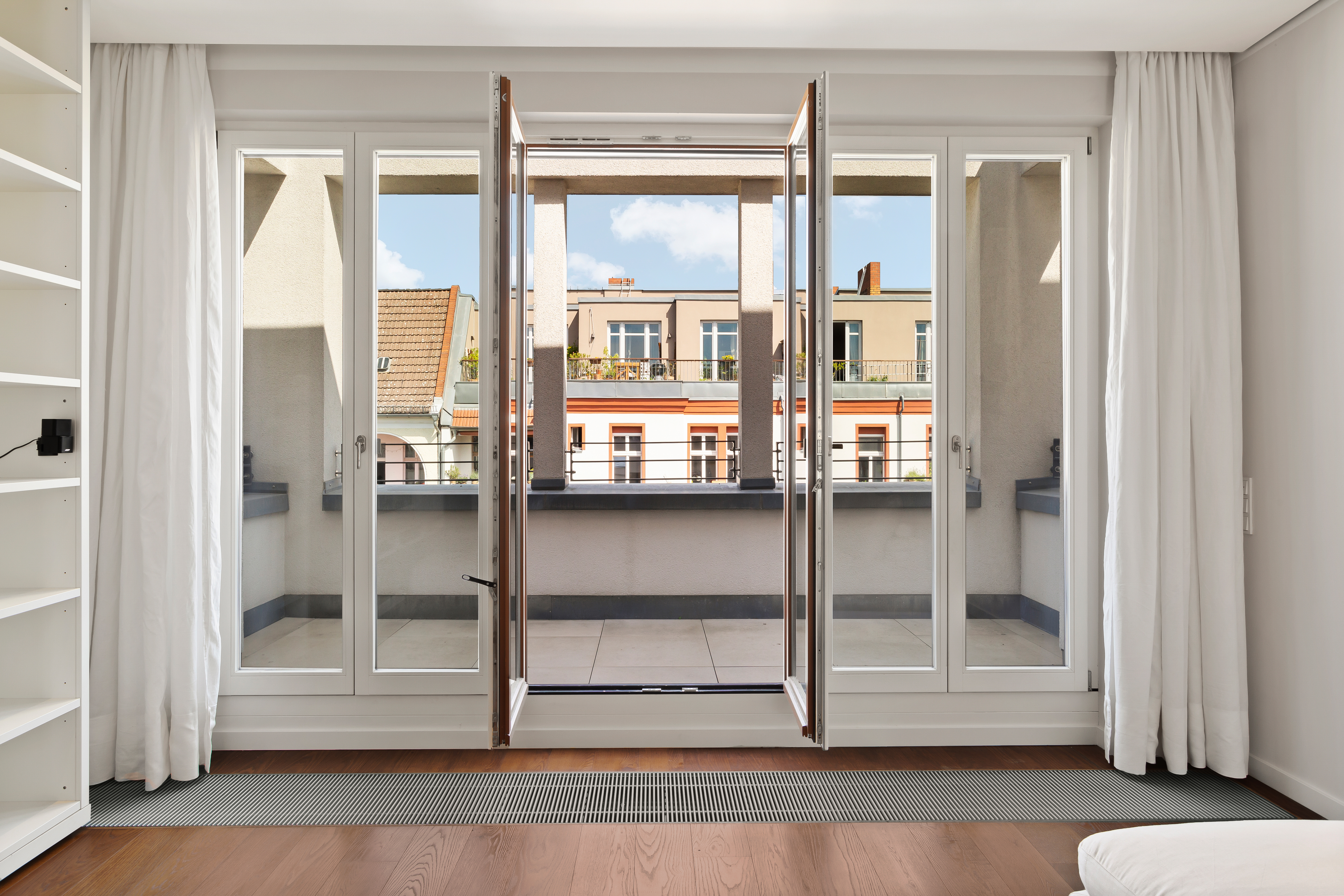 Helles Zimmer mit Holzboden, bodentiefen Fenstern und Zugang zu einem Balkon.