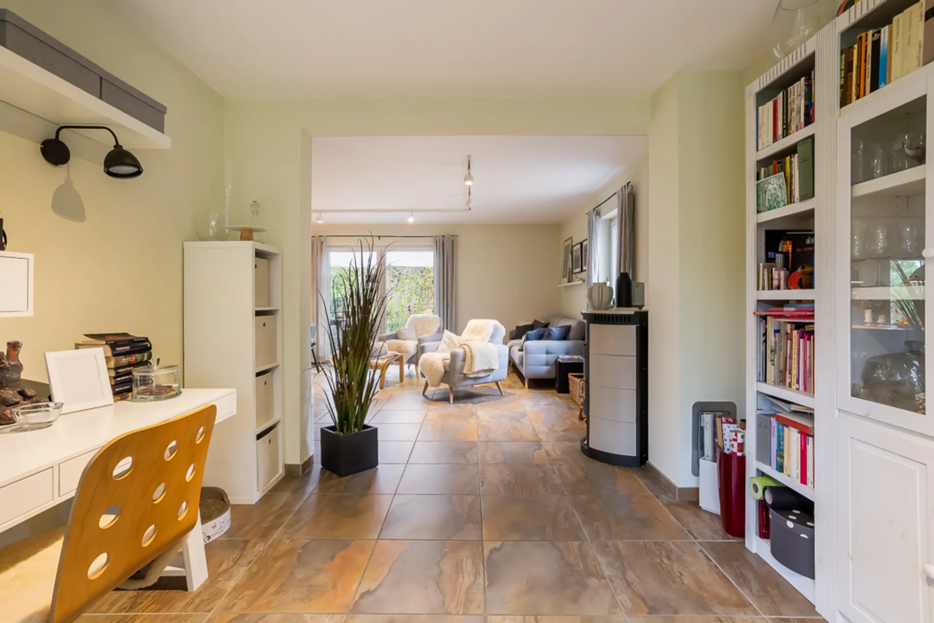 Helles Wohnzimmer mit Schreibtisch, Bücherregalen, Sesseln und großer Fensterfront.
