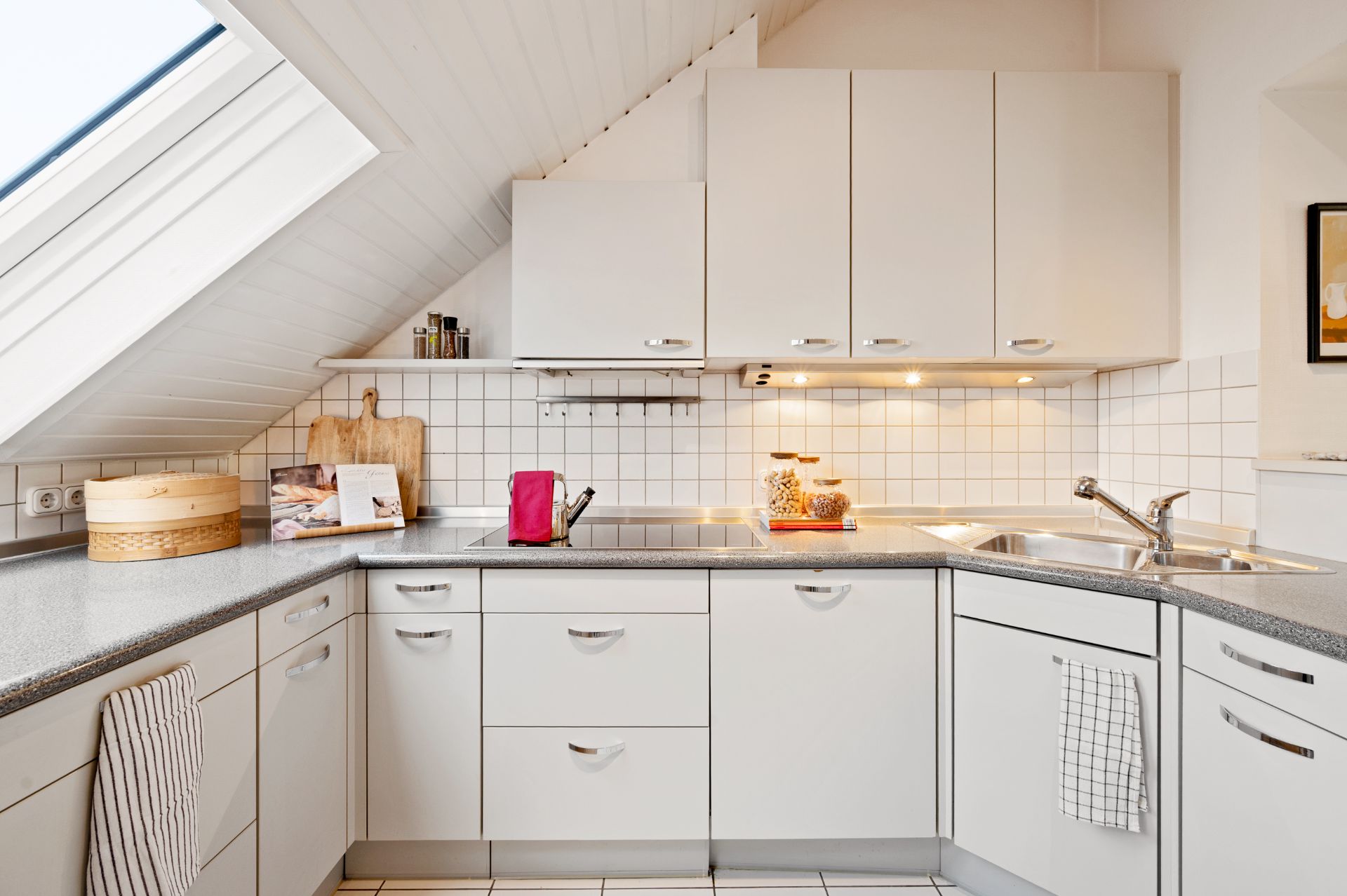 Helle Einbauküche mit weißen Schränken, Dachfenster und modernem Waschbecken.