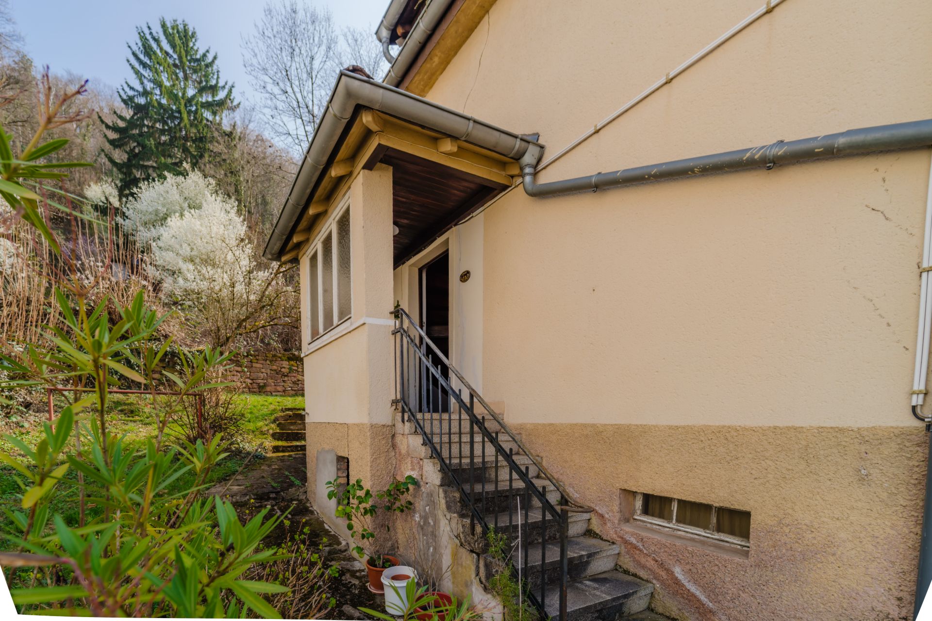 Außentreppe führt zum Hauseingang, daneben Garten mit Sträuchern und Bäumen.