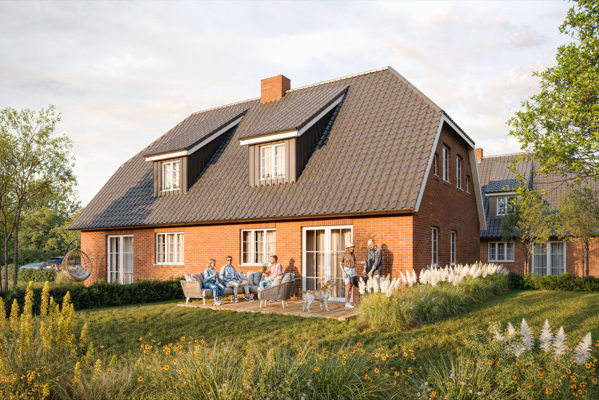 Backstein-Einfamilienhaus mit Terrasse, Menschen sitzen und stehen im Garten.