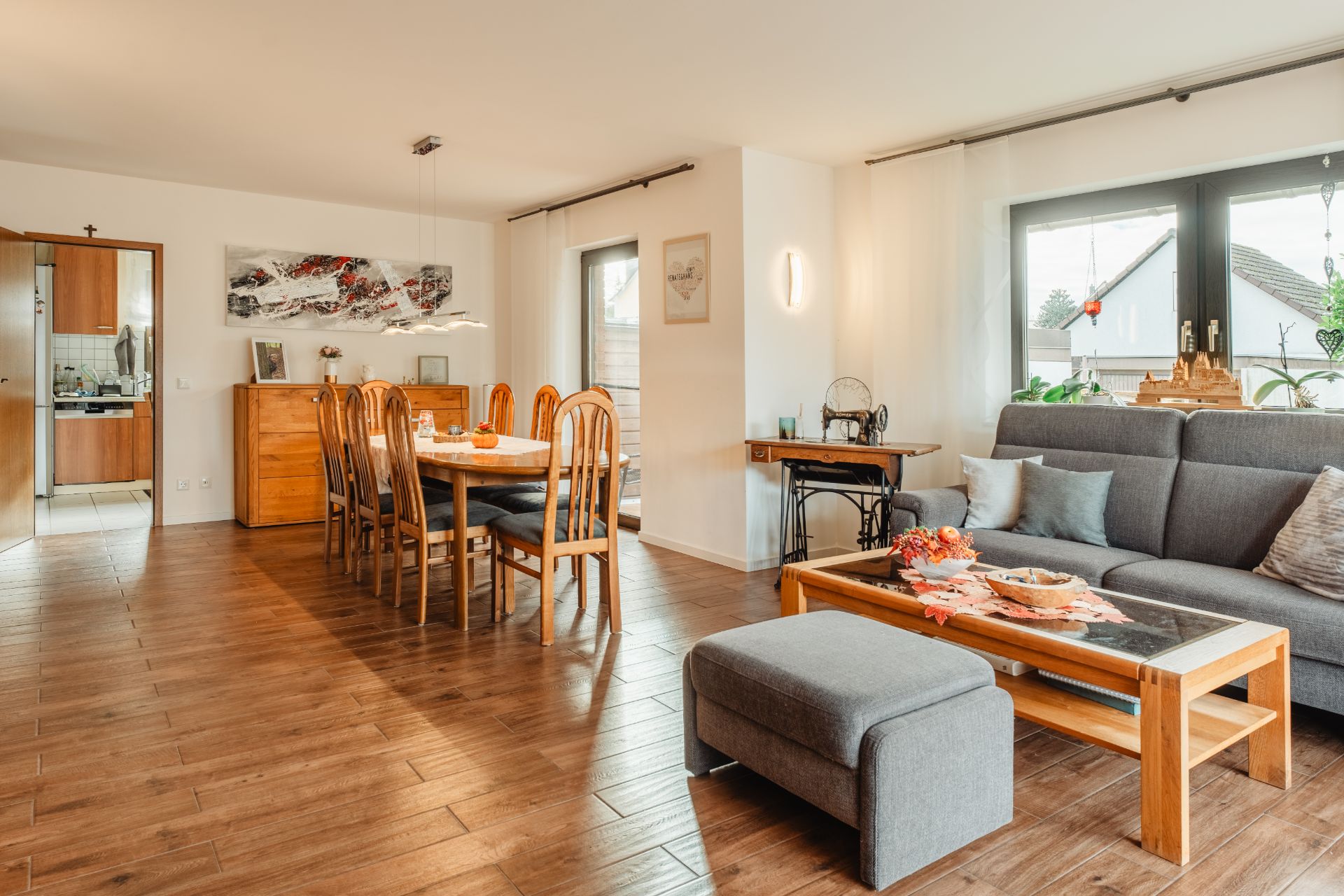 Helles Wohnzimmer mit grauem Sofa, Holztisch, Essbereich und Blick in die Küche.