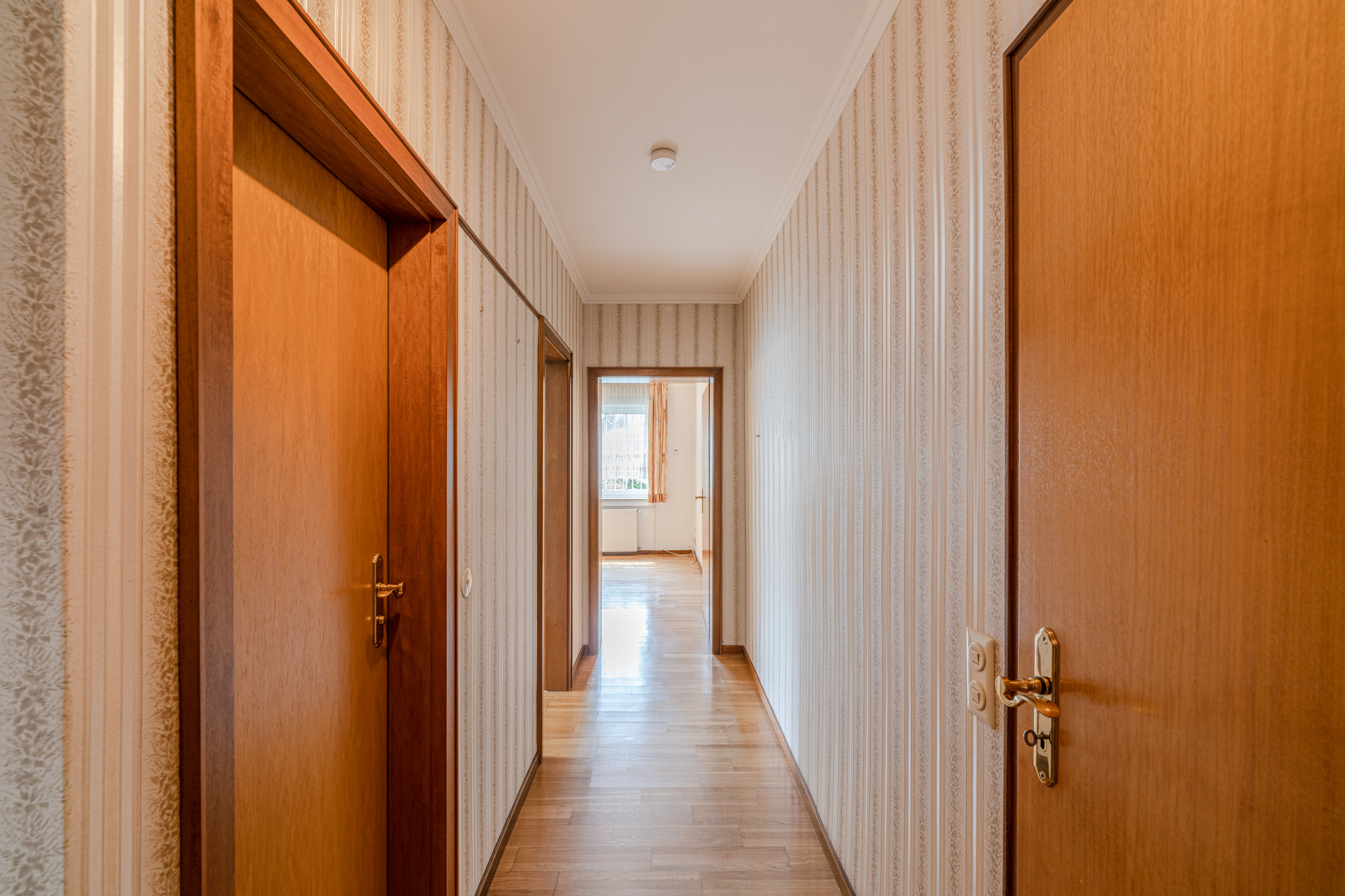 Heller Flur mit Holztüren und gestreifter Tapete in einer Wohnung.