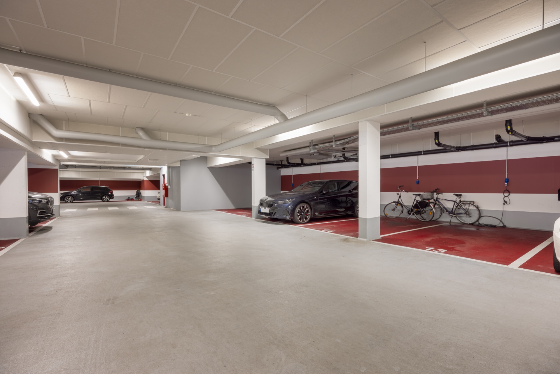 Helle Tiefgarage mit geparkten Autos und Fahrrädern an markierten Stellplätzen.