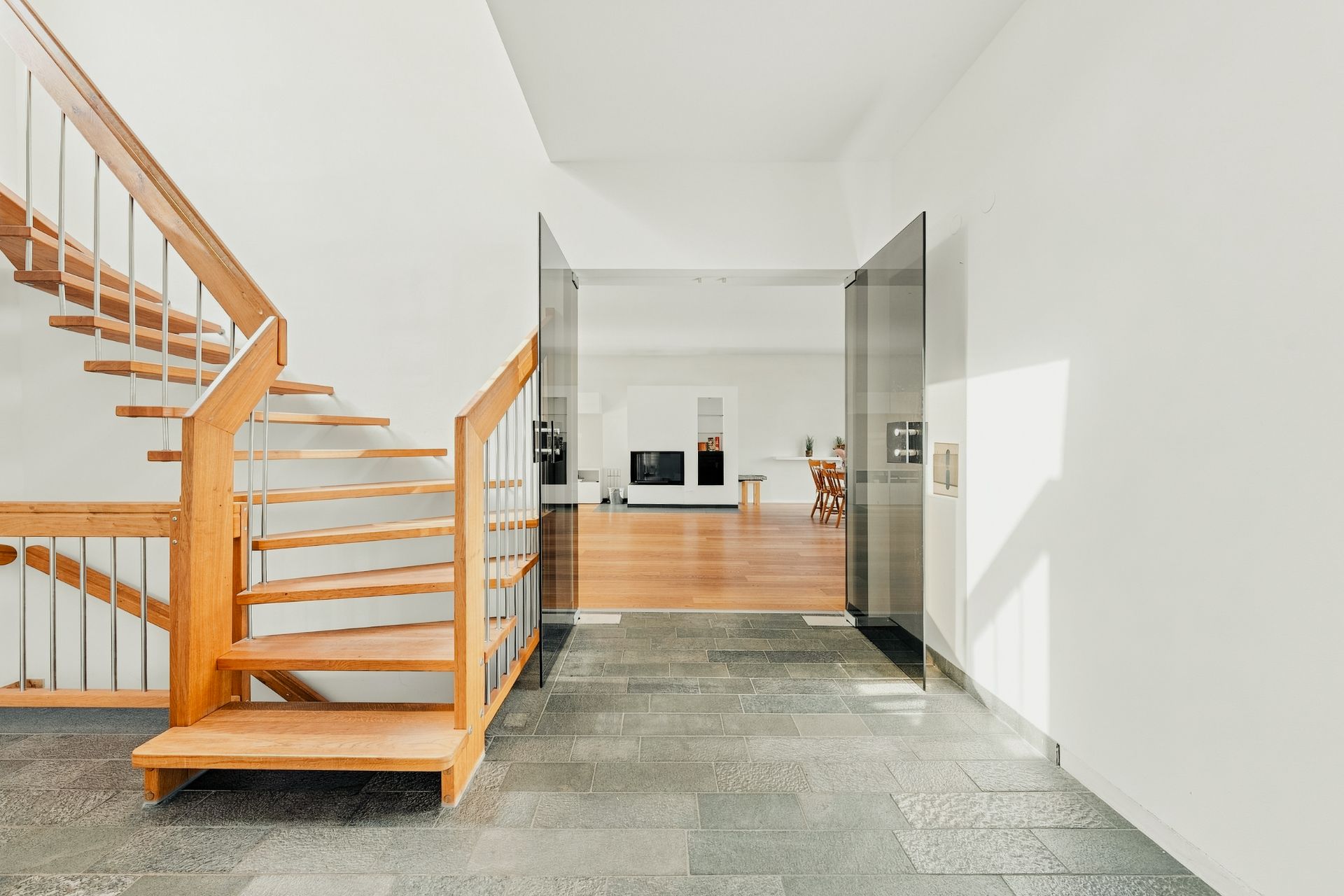 Heller Flur mit Holztreppe, Fliesenboden und Blick ins Wohnzimmer mit Holzboden.