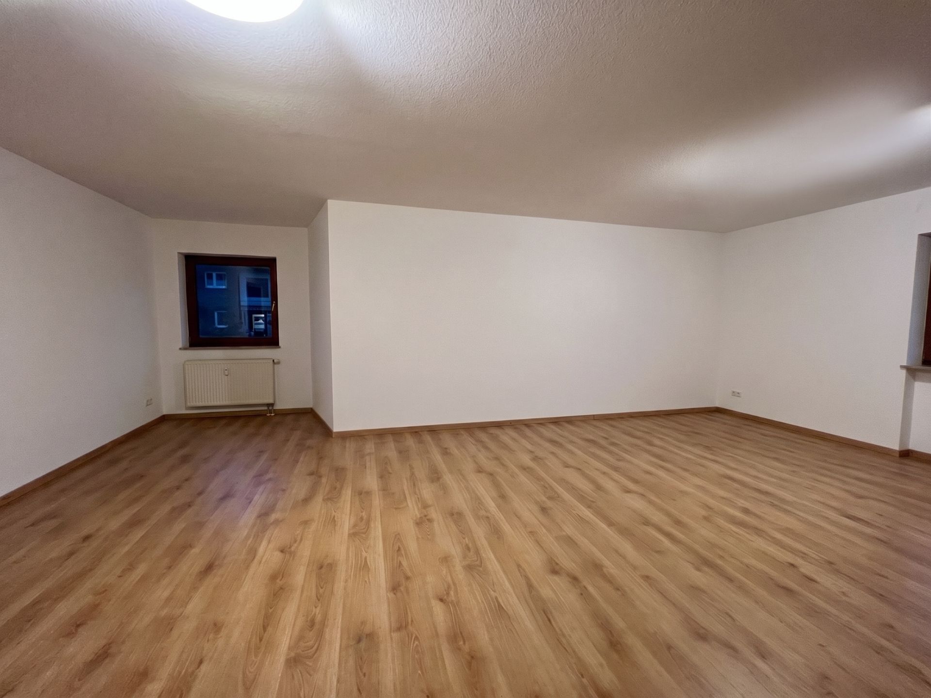 Leeres Zimmer mit hellem Holzfußboden, weißen Wänden und zwei Fenstern.